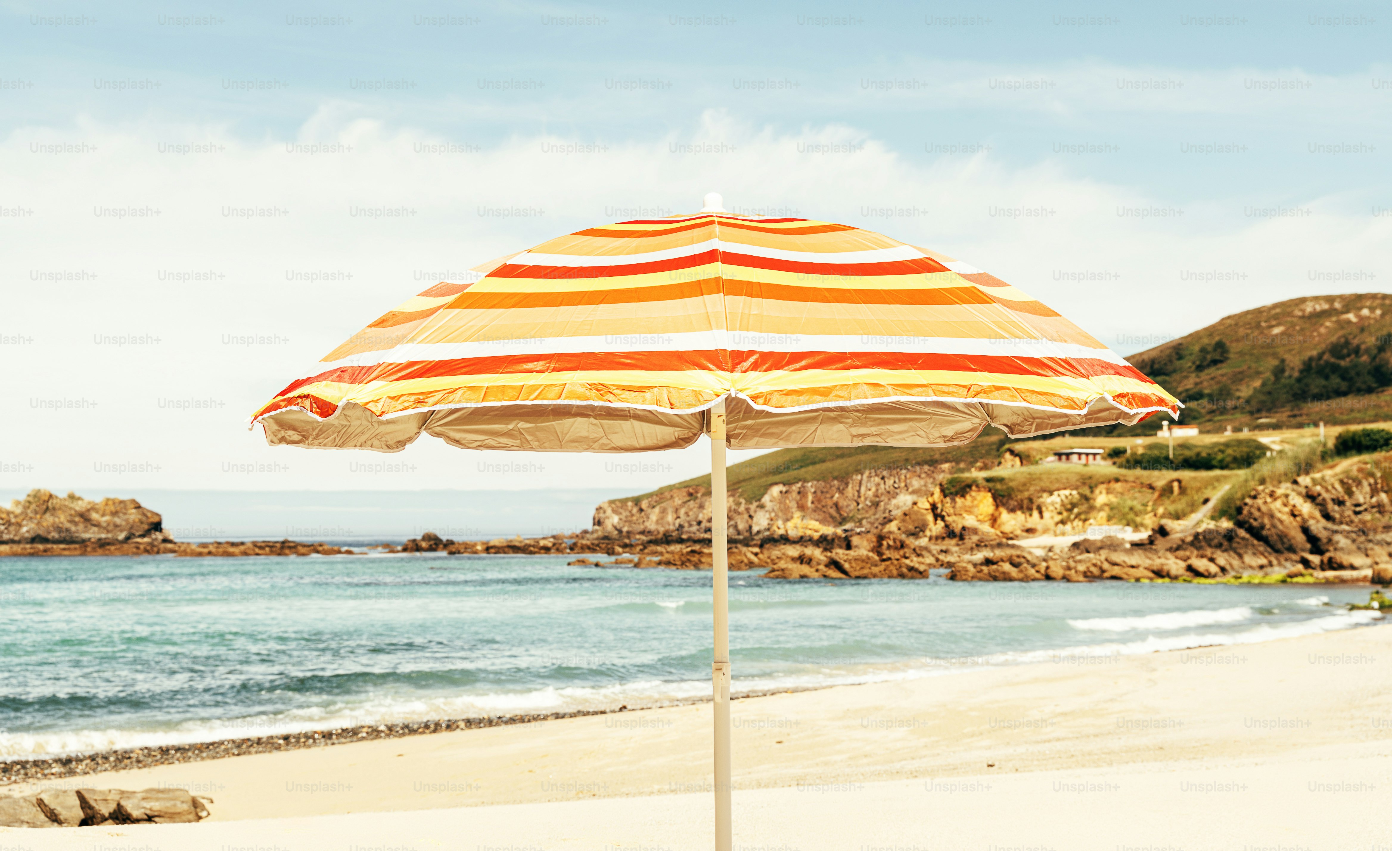 Striped beach umbrella on sandy shore by rocky coast