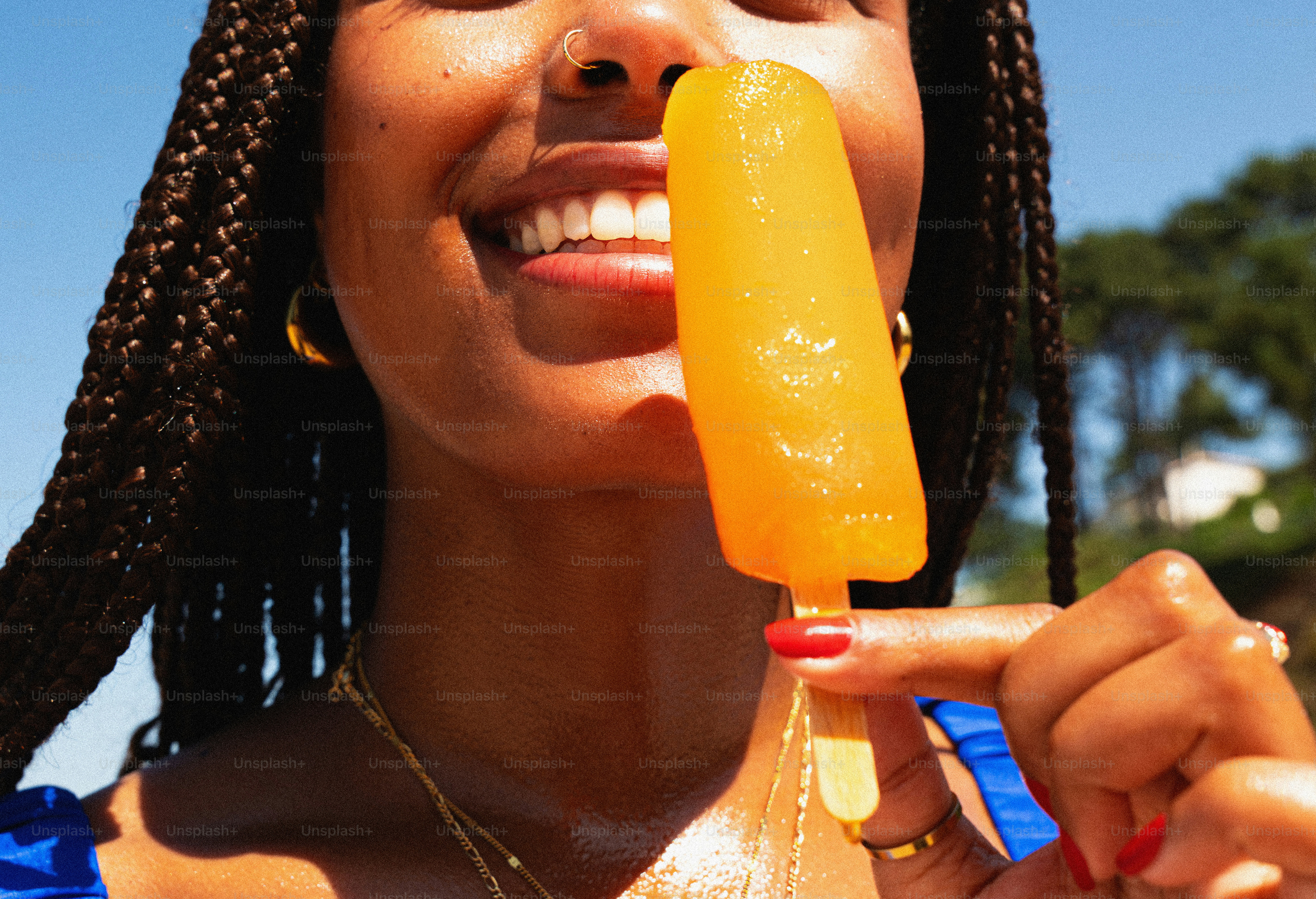 Woman with braids smiling, holding orange popsicle