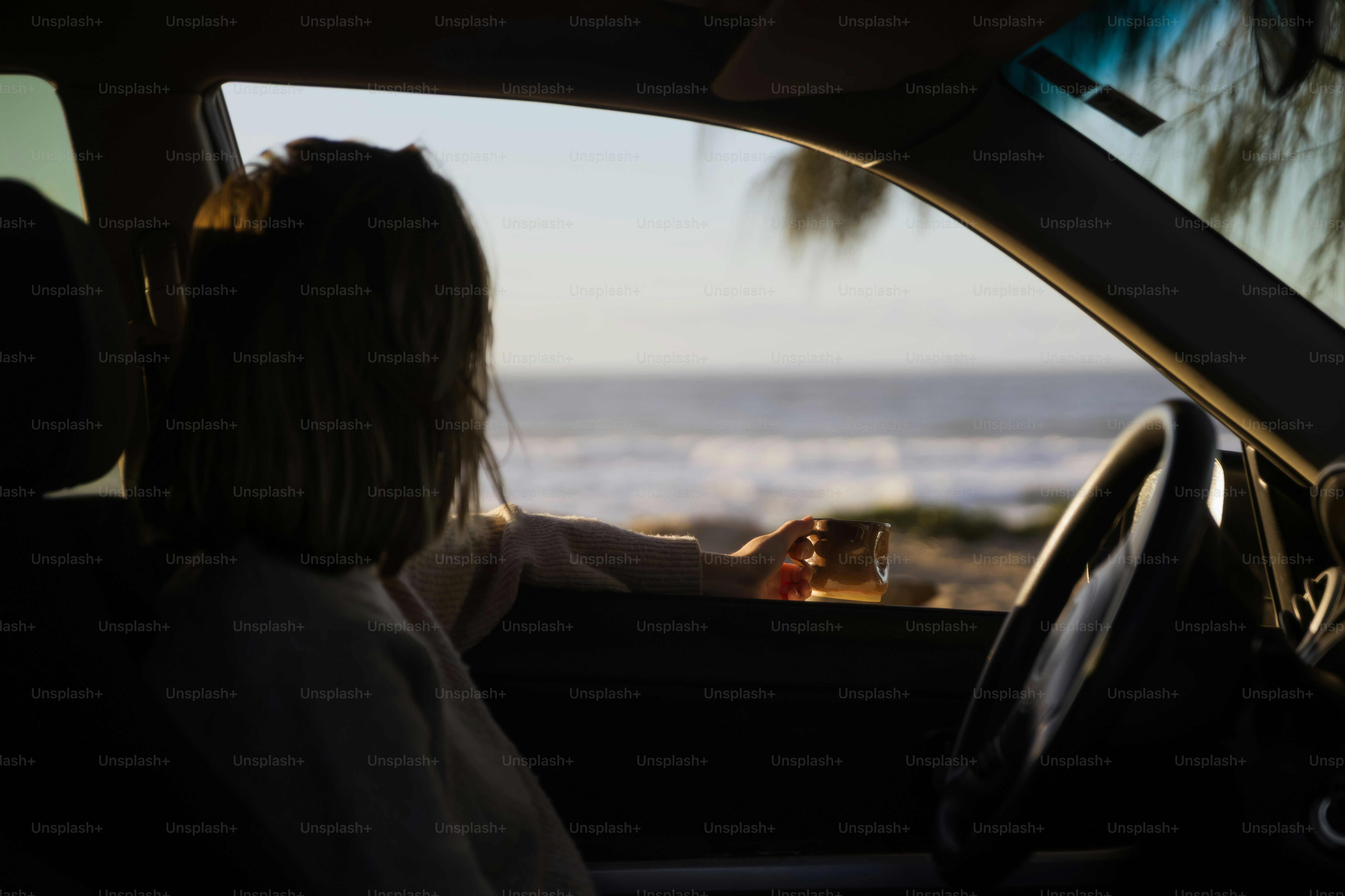 Person holding beverage looking at ocean from car