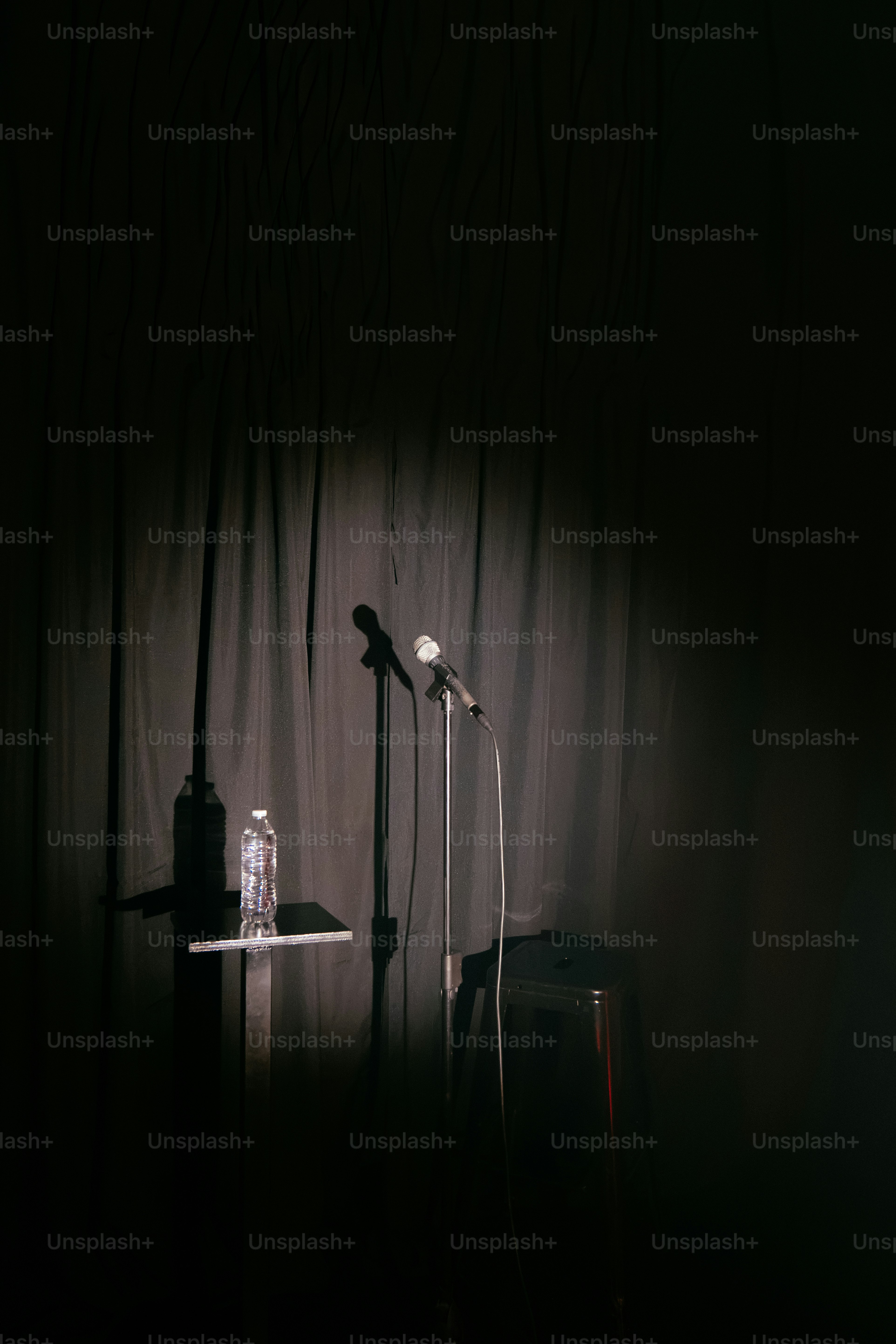 Spotlight illuminates two microphones and water bottle on stage