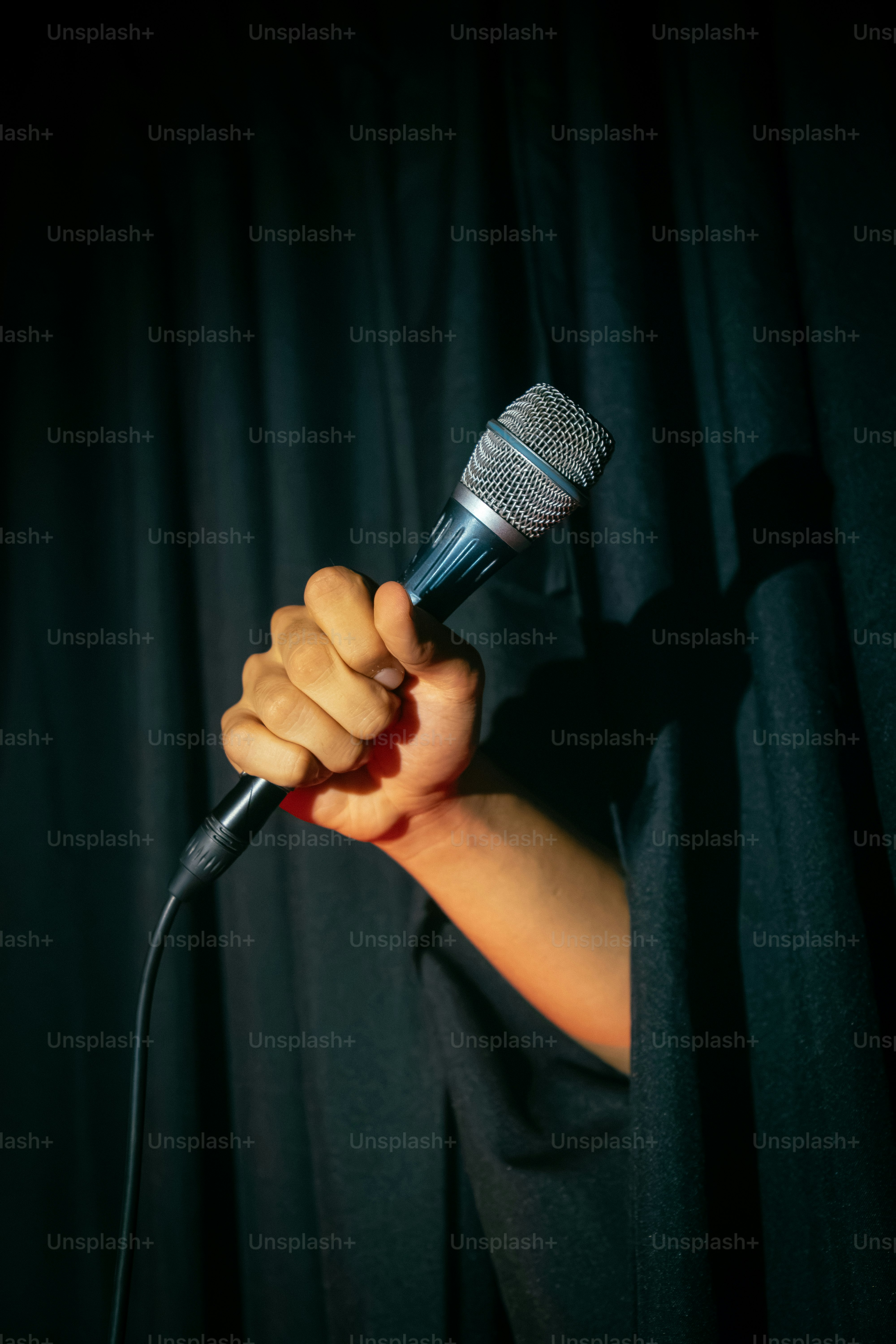 Hand holding microphone emerges from dark stage curtain