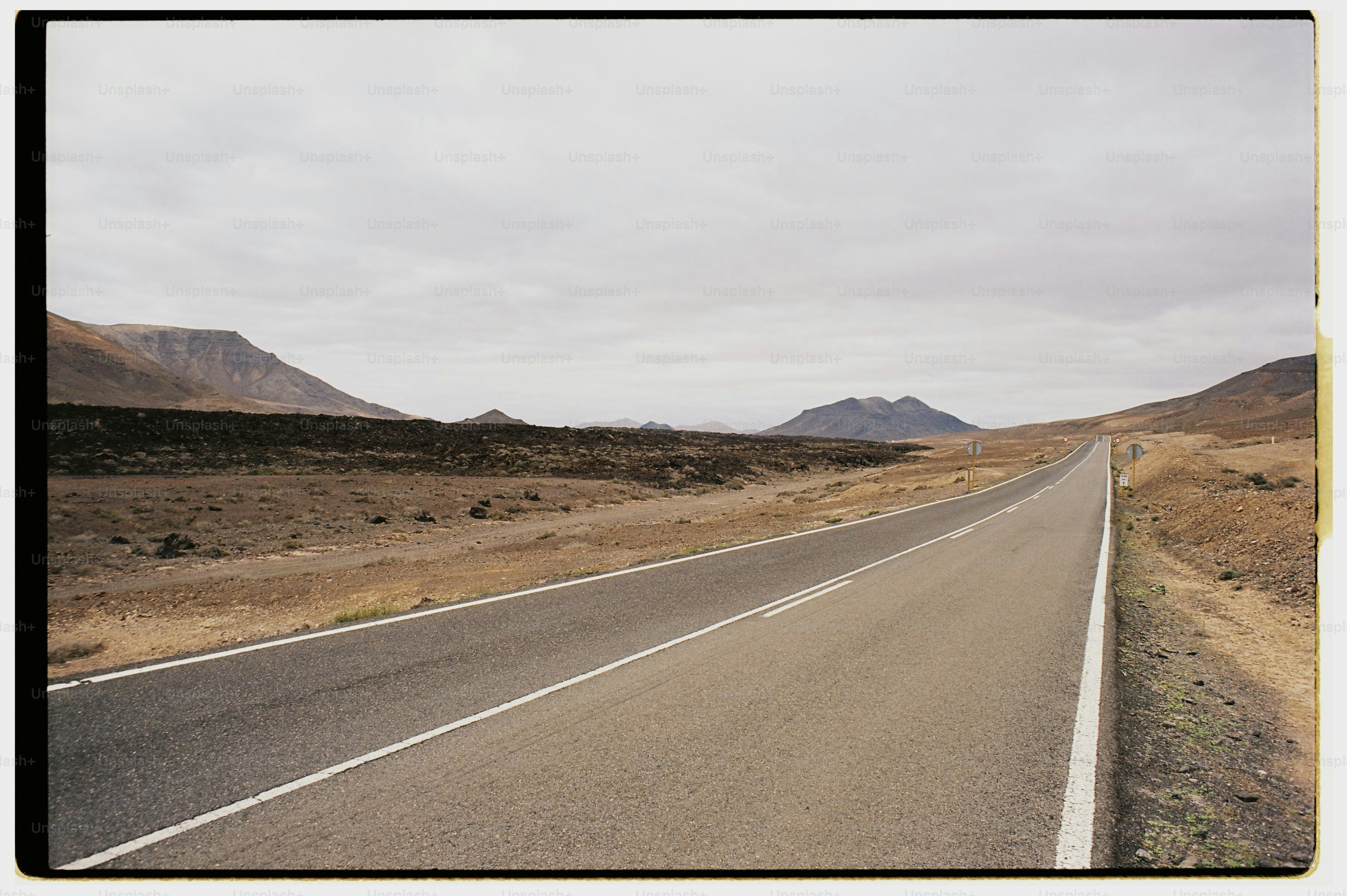 Empty road in barren landscape under cloudy sky