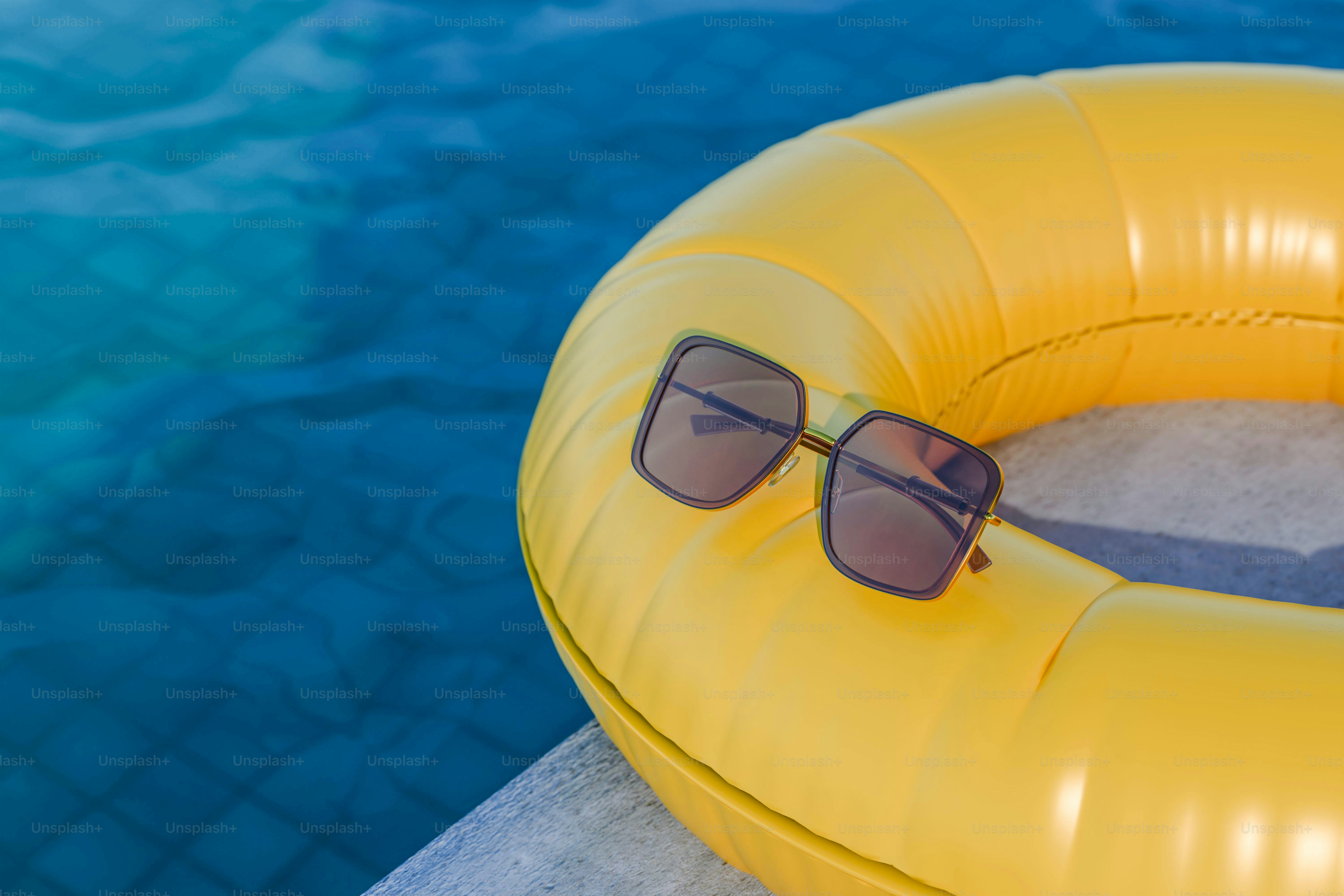 Sunglasses resting on yellow inflatable ring by pool