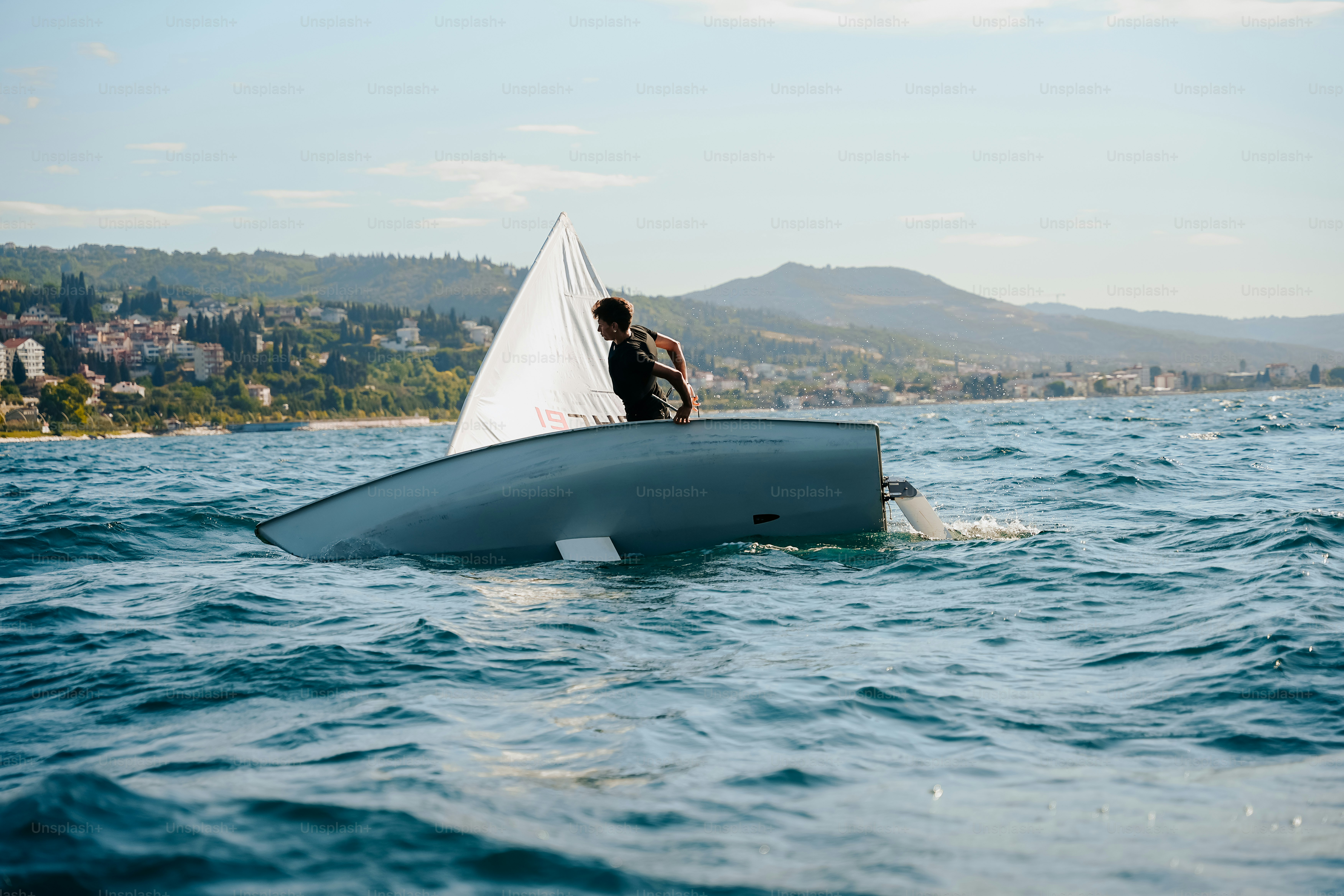 Person with capsized sailboat in wavy blue water