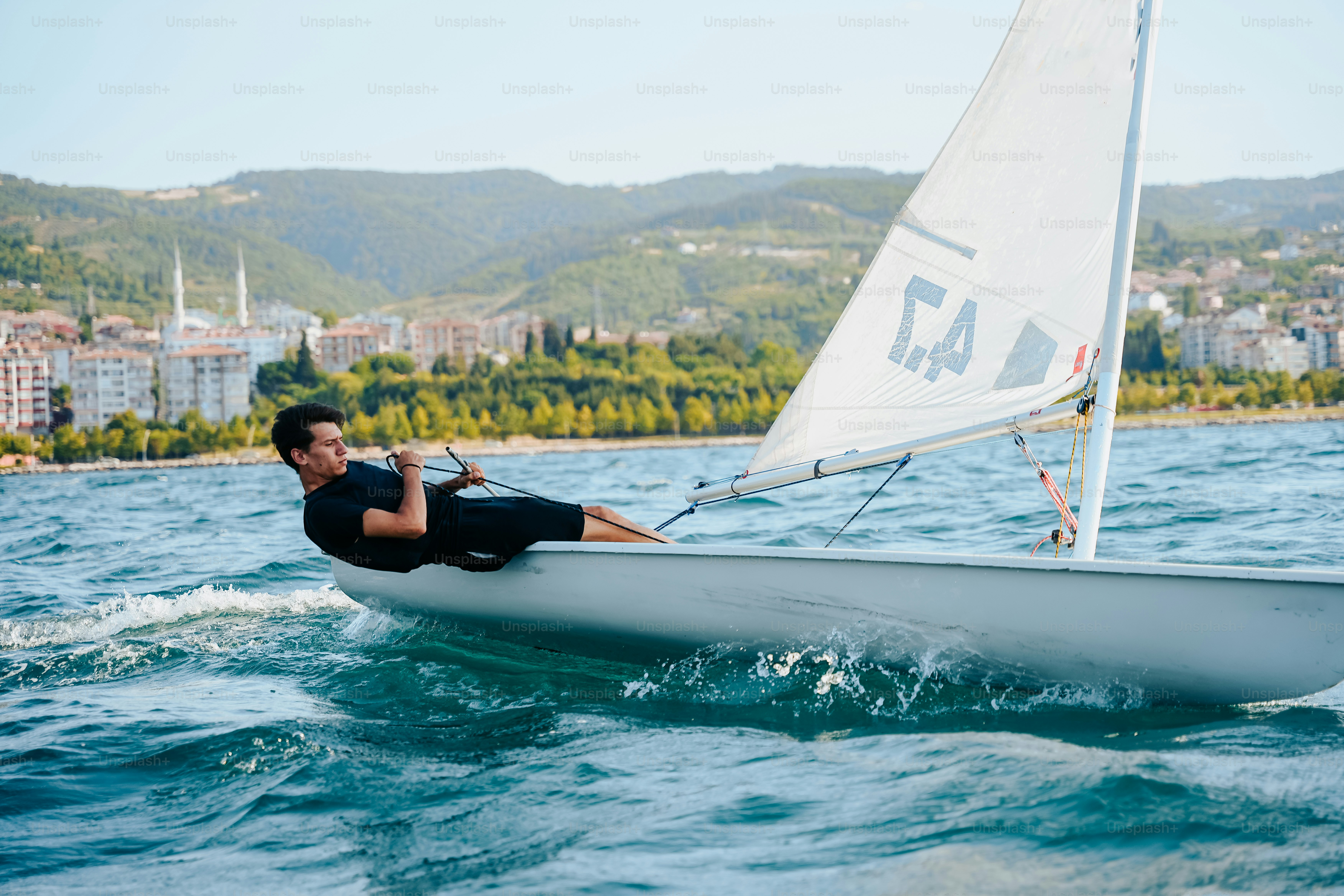Man sailing a small sailboat with coastal town background
