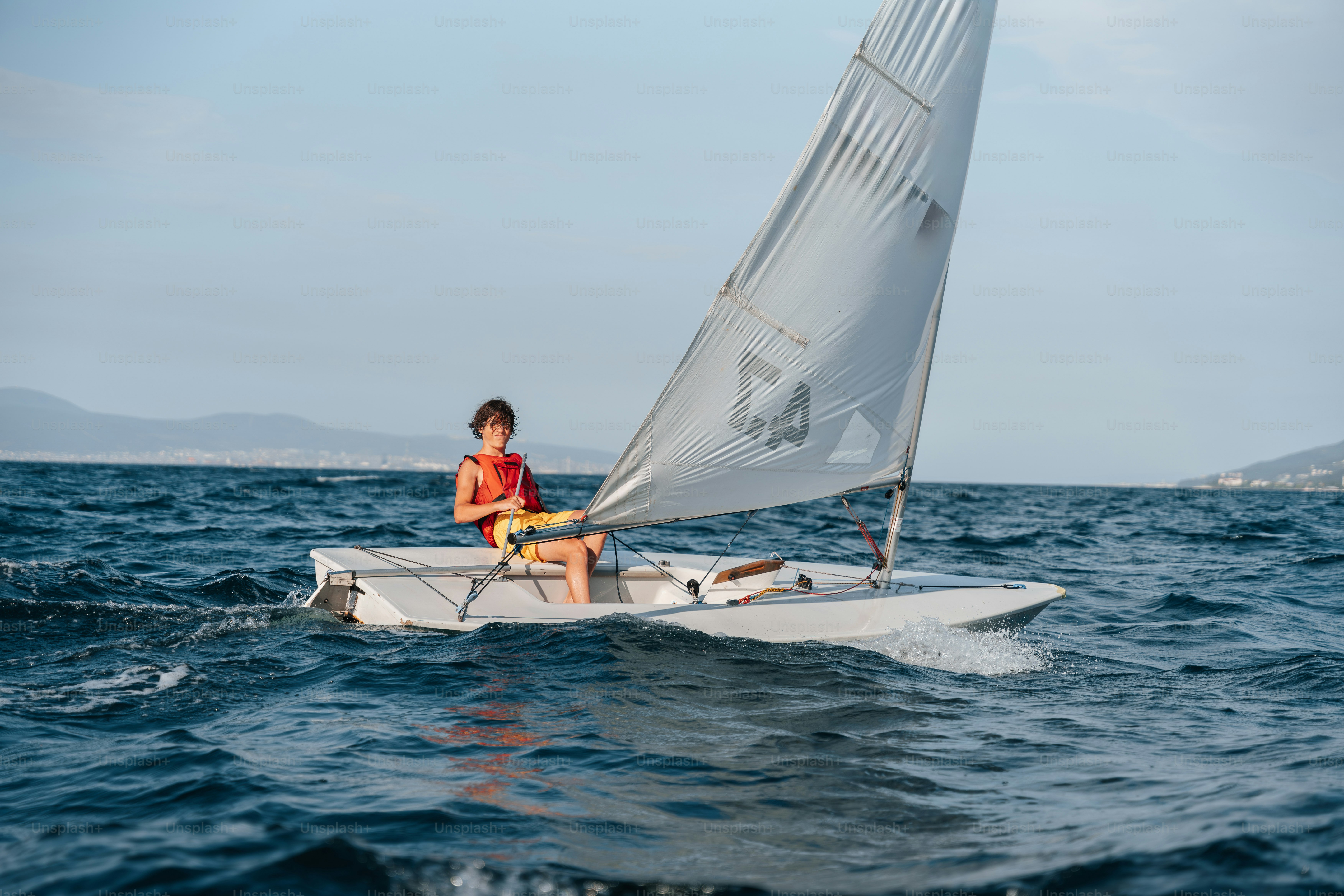 Person sailing small sailboat on blue wavy water