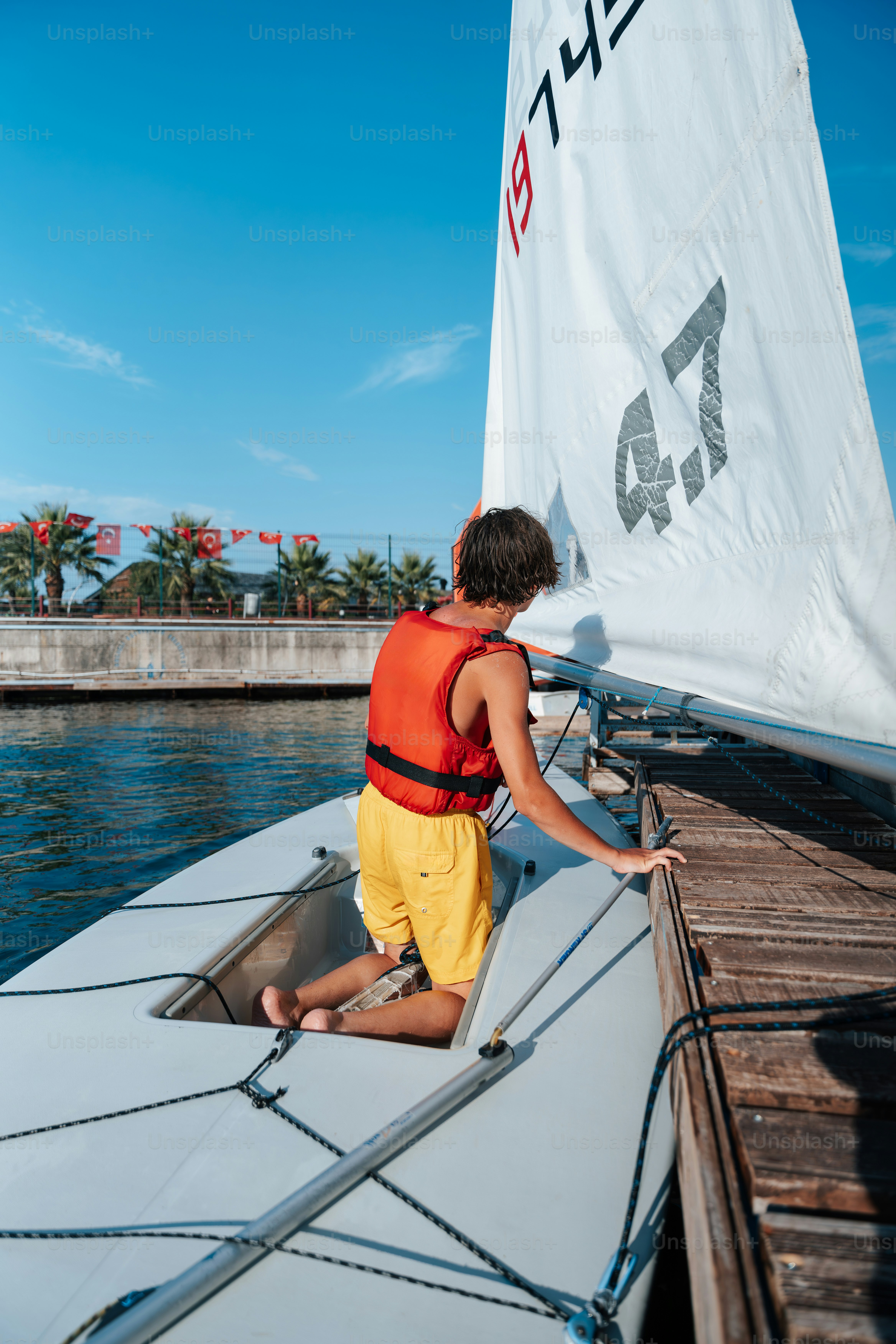 Person in life vest boarding sailboat from wooden dock