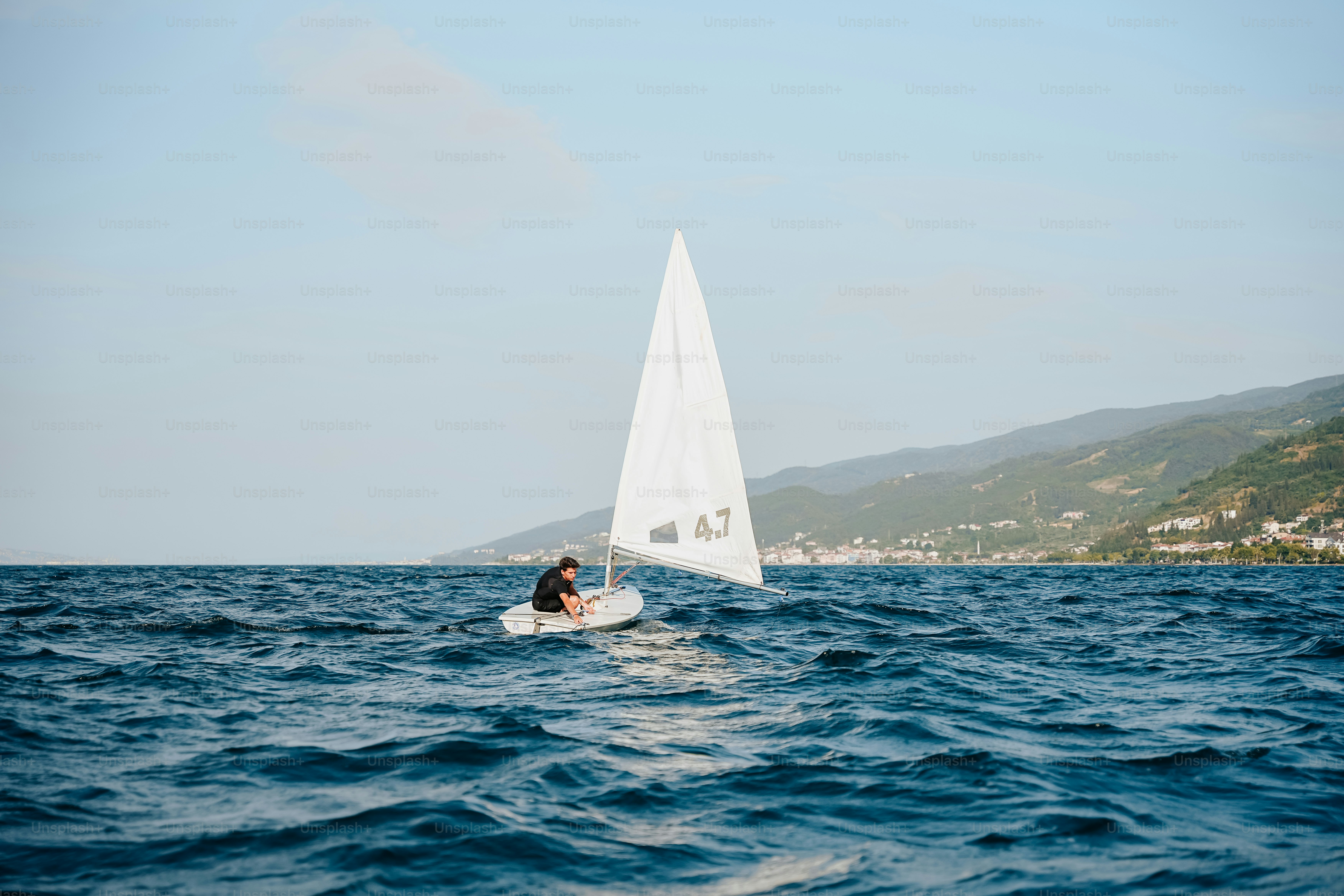 Sailor on small sailboat with distant coastline