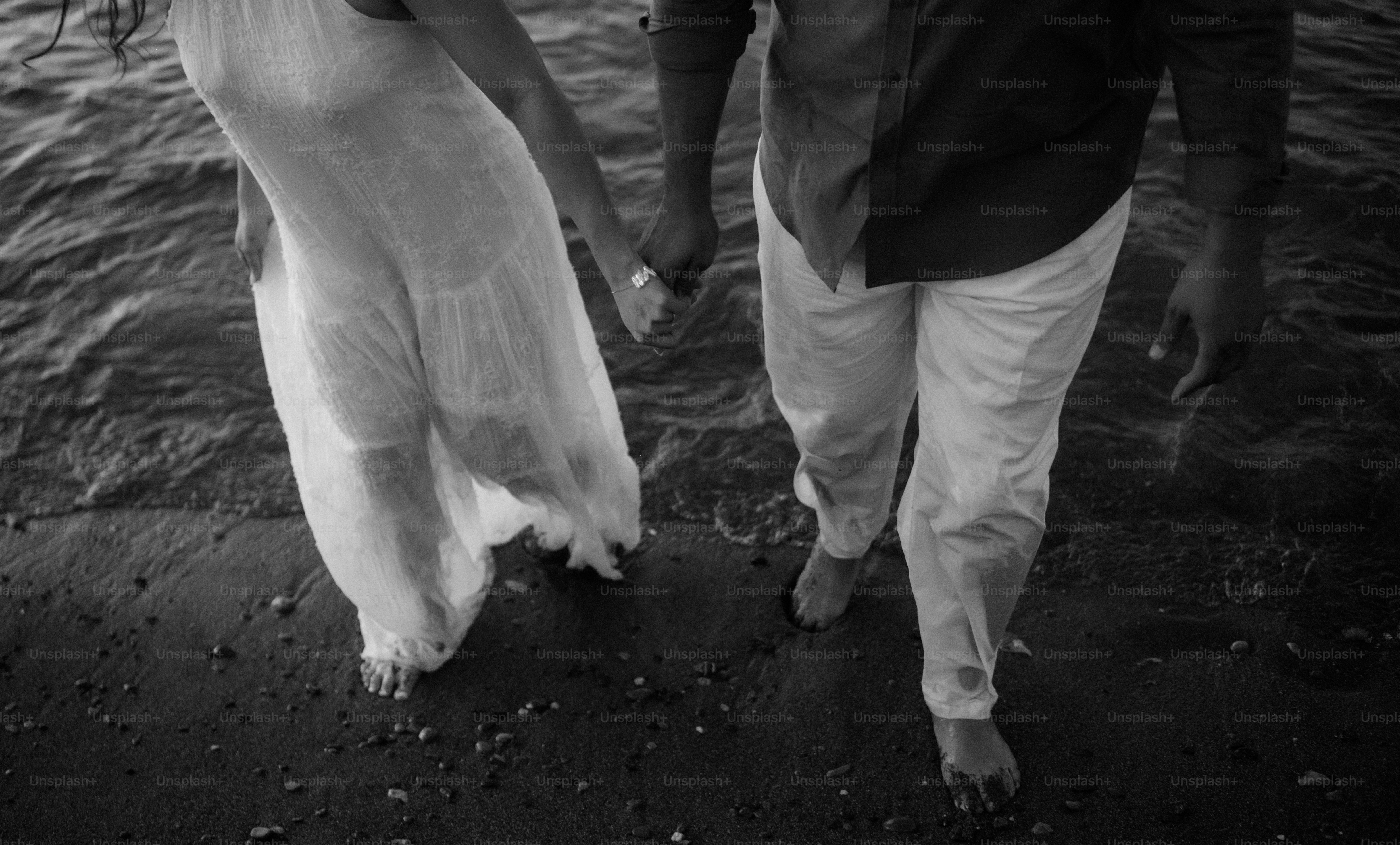 Casal de mãos dadas andando descalço à beira da água