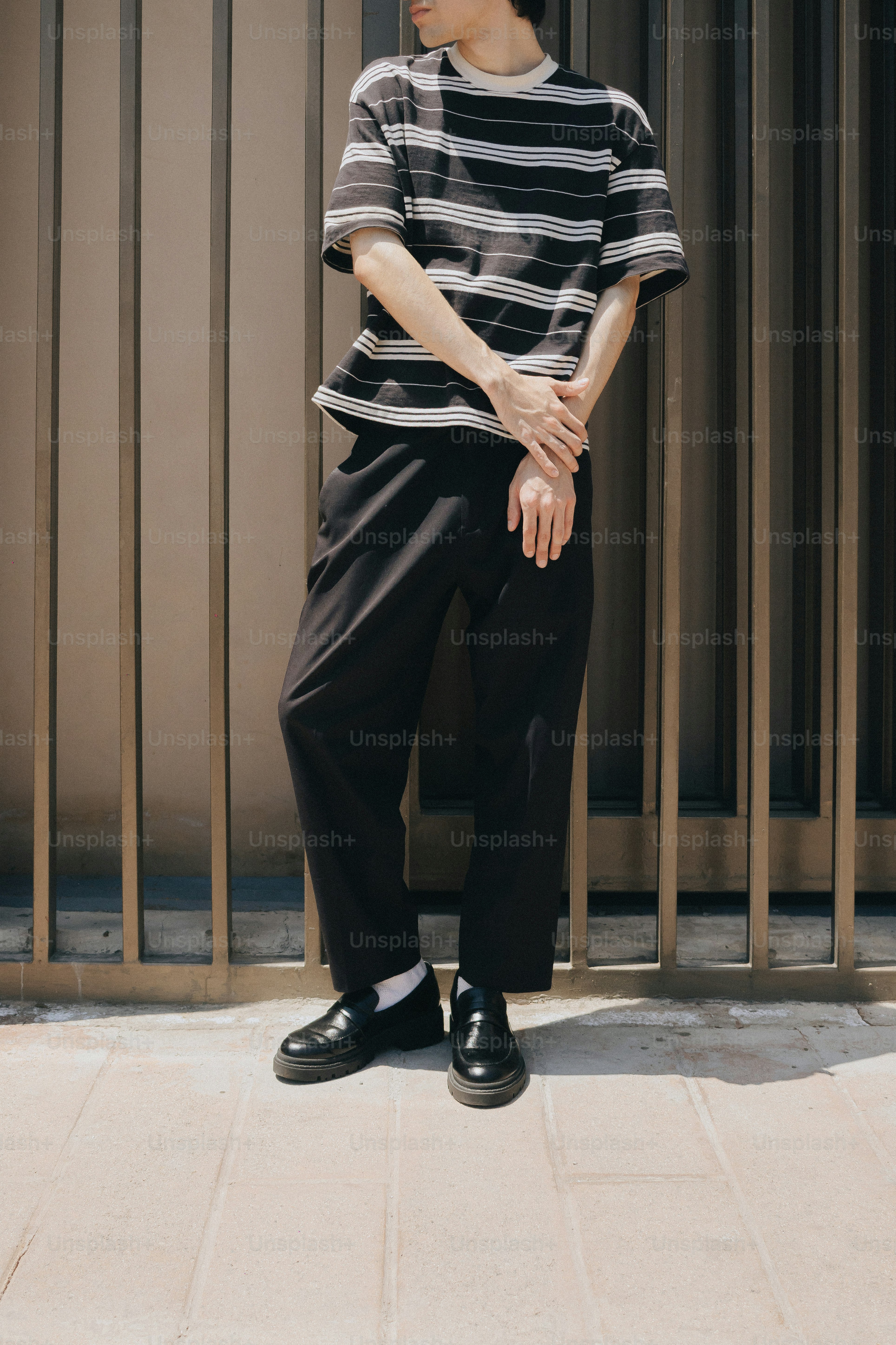 Person in striped t-shirt, black pants against wall