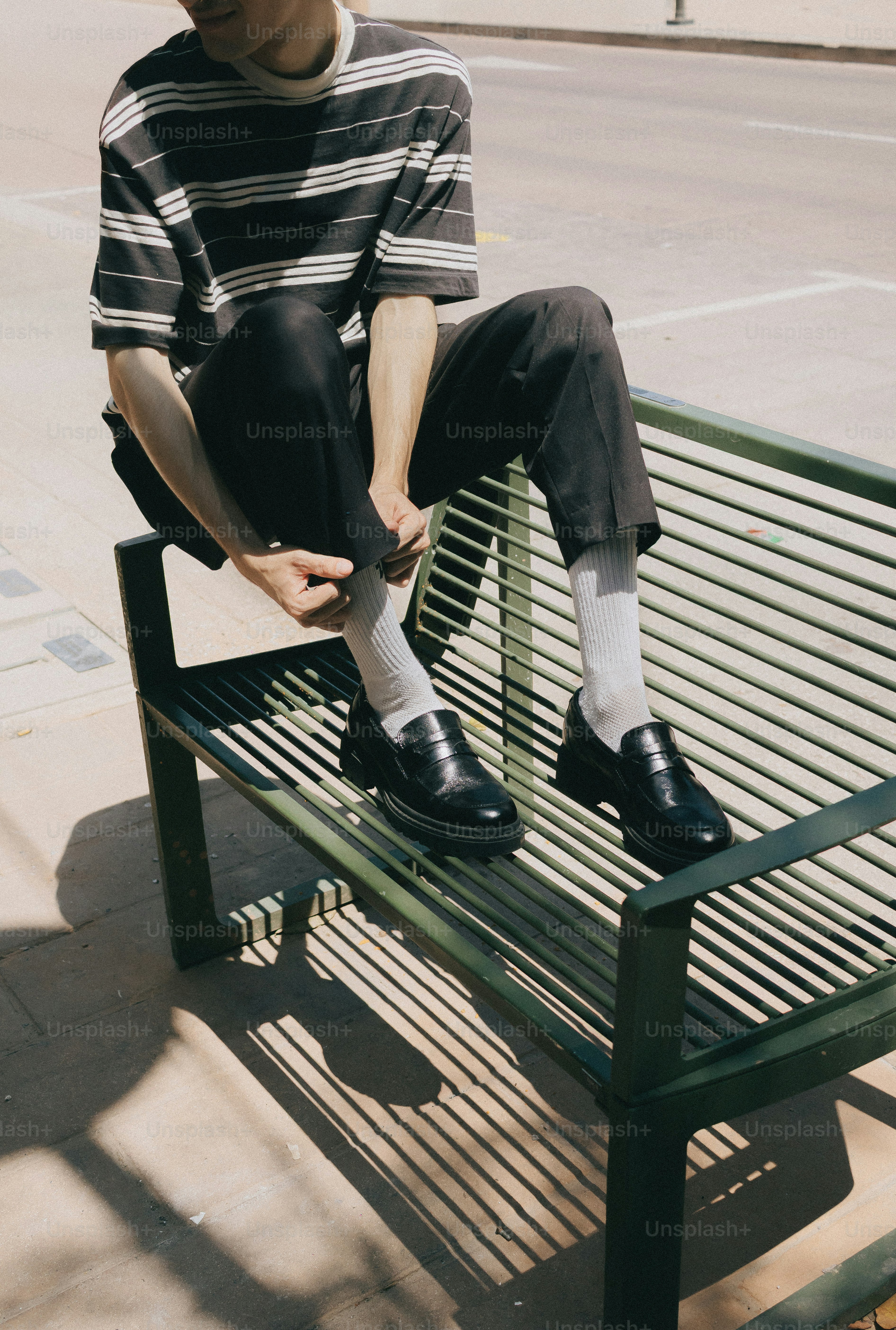 Person adjusting pants while sitting on green bench