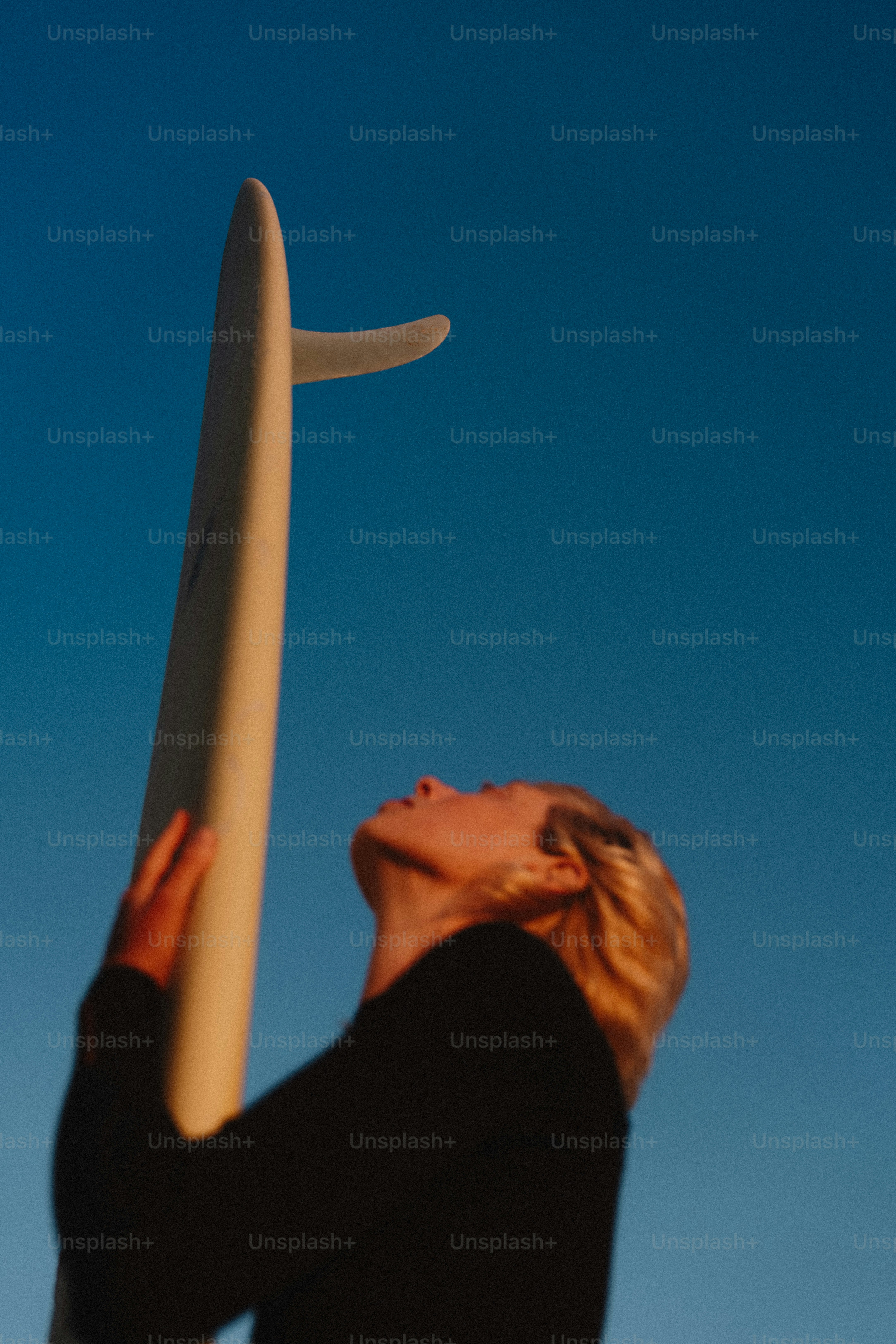 Surfer holding surfboard, looking up at blue sky