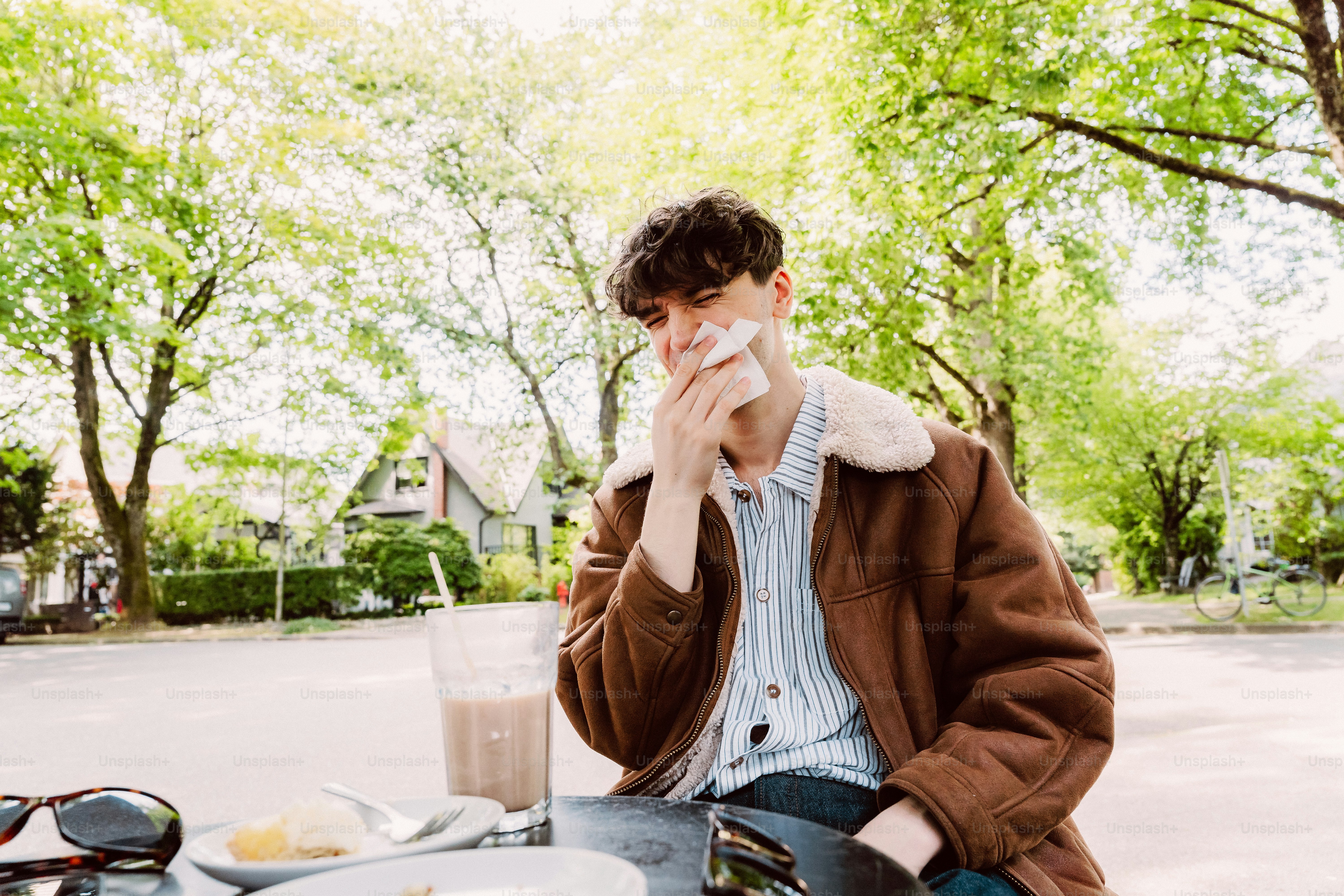 Man wiping nose with tissue at outdoor table