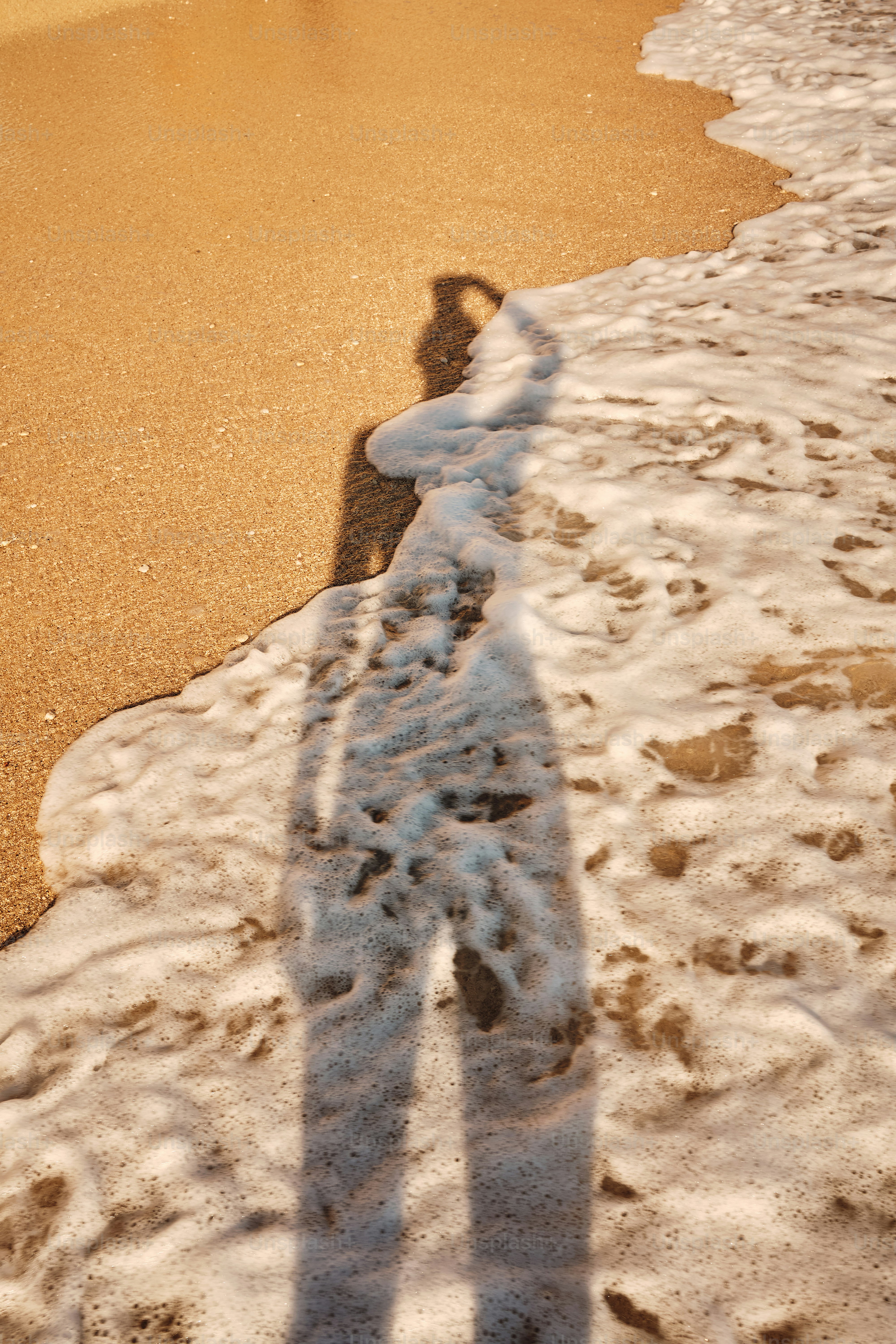 Person's shadow on sandy beach with foamy ocean waves