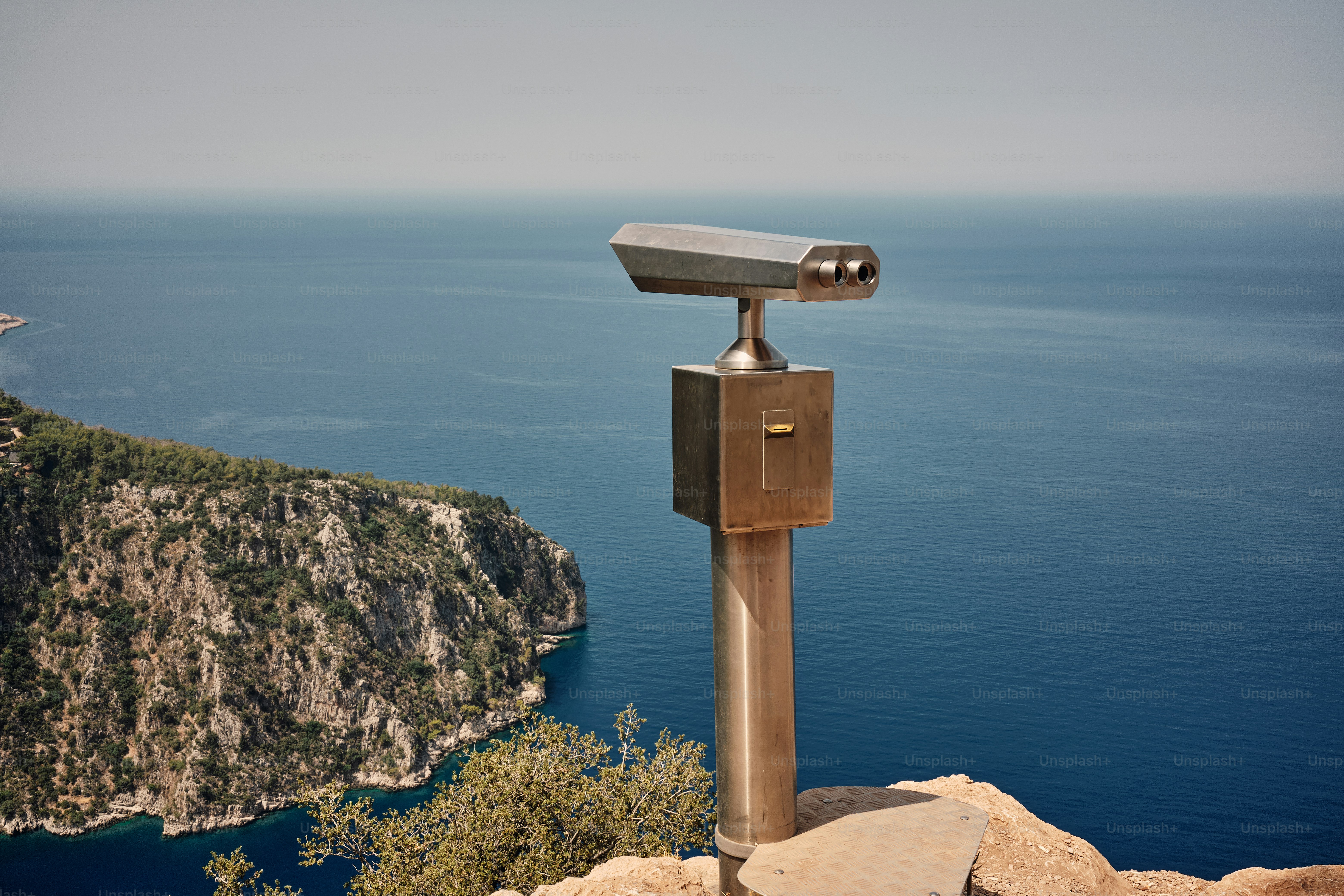 Coin-operated telescope overlooking blue sea from cliff