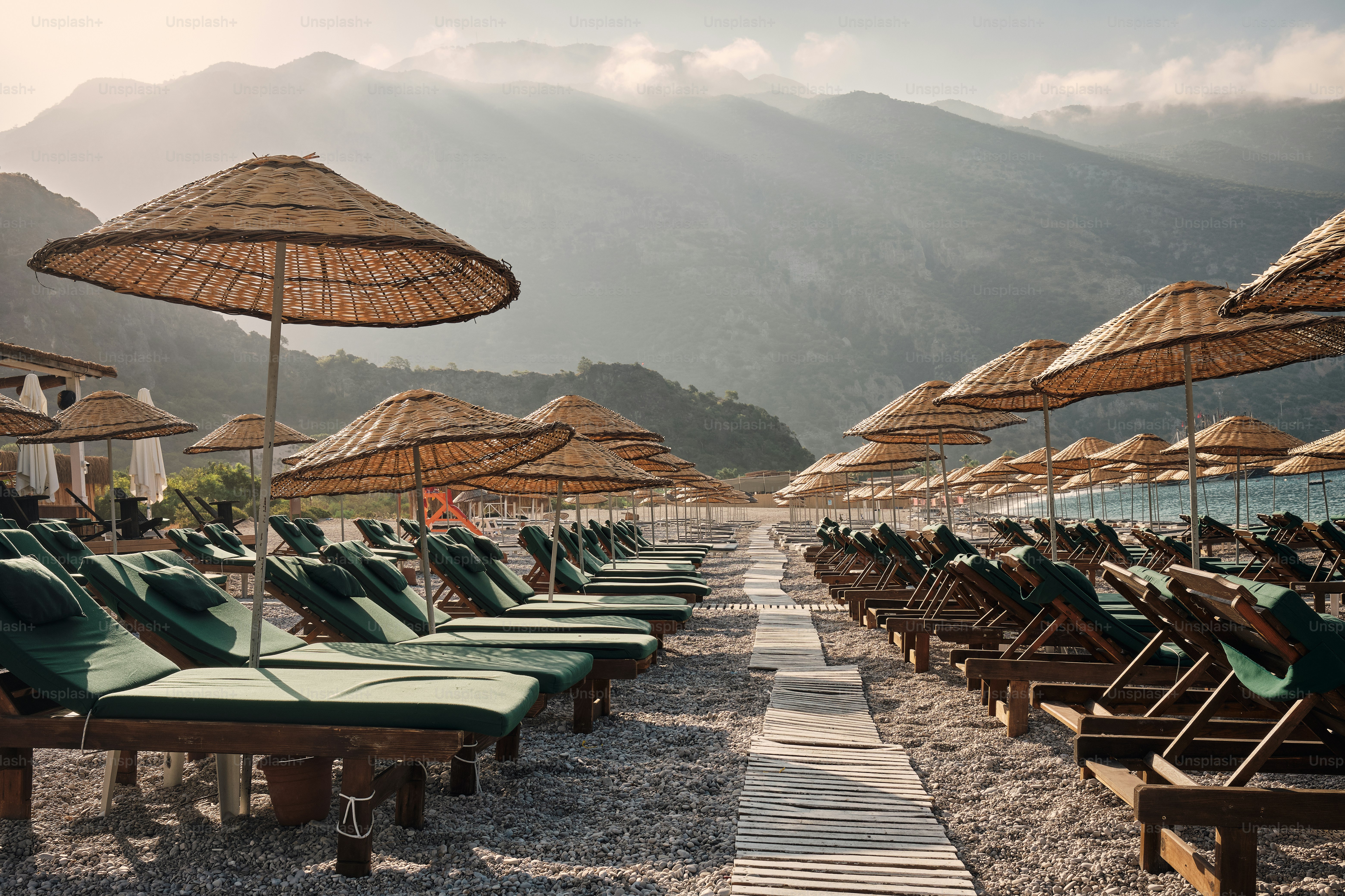 Beach with lounge chairs, straw umbrellas, and mountains