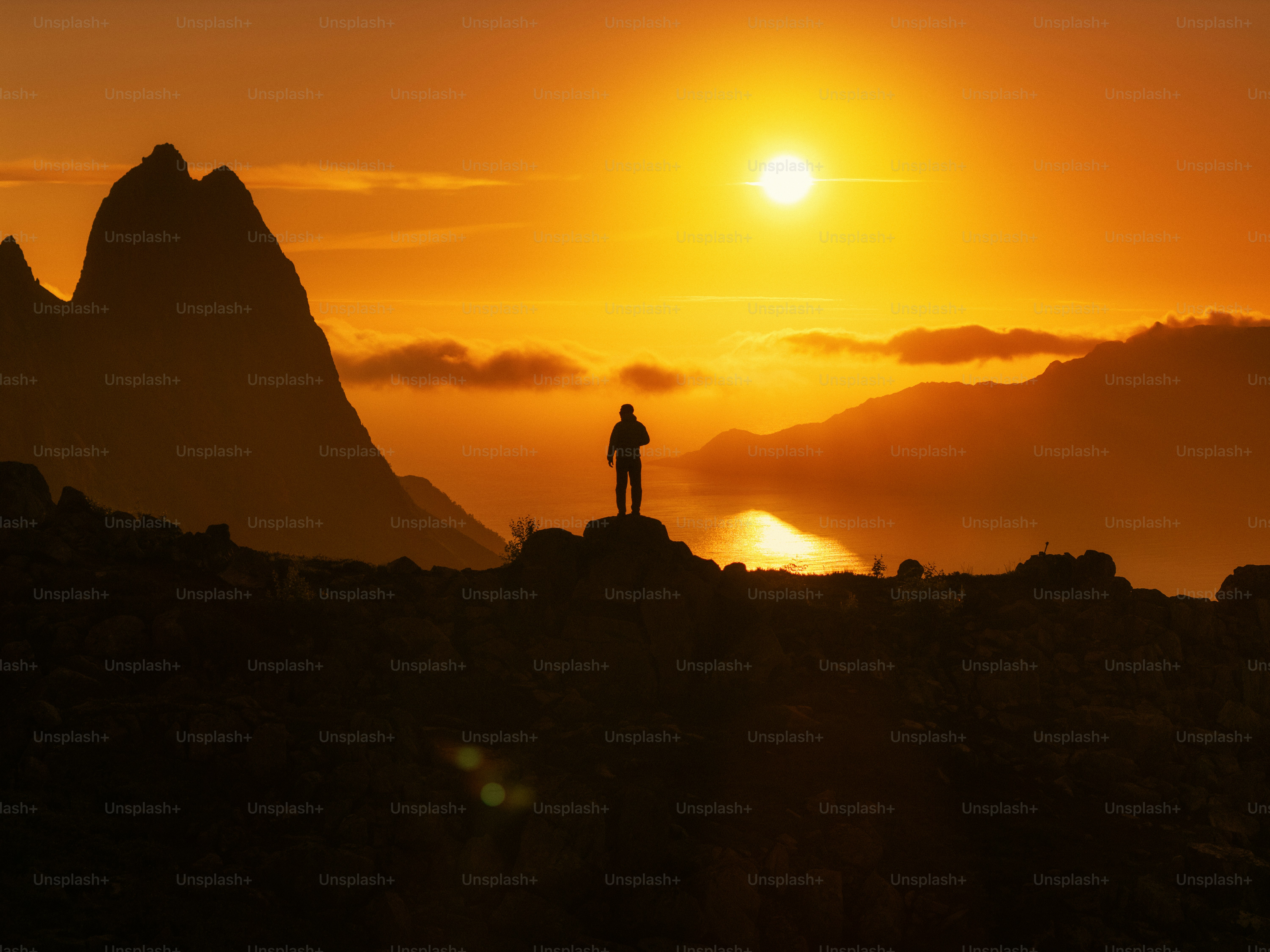 Lone figure watching vibrant sunset over mountains