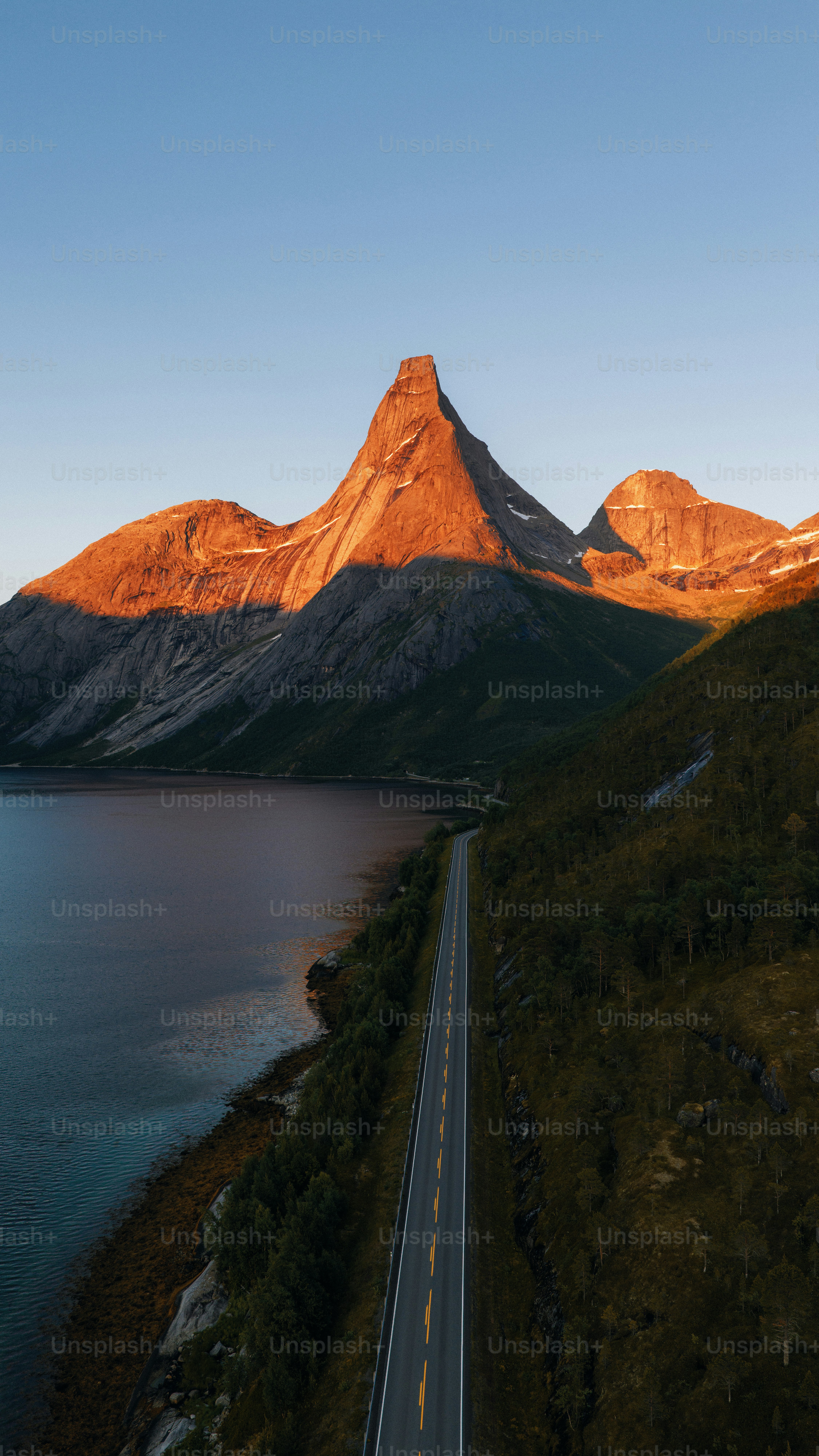 Sunlit mountain peak, road, and water at sunset
