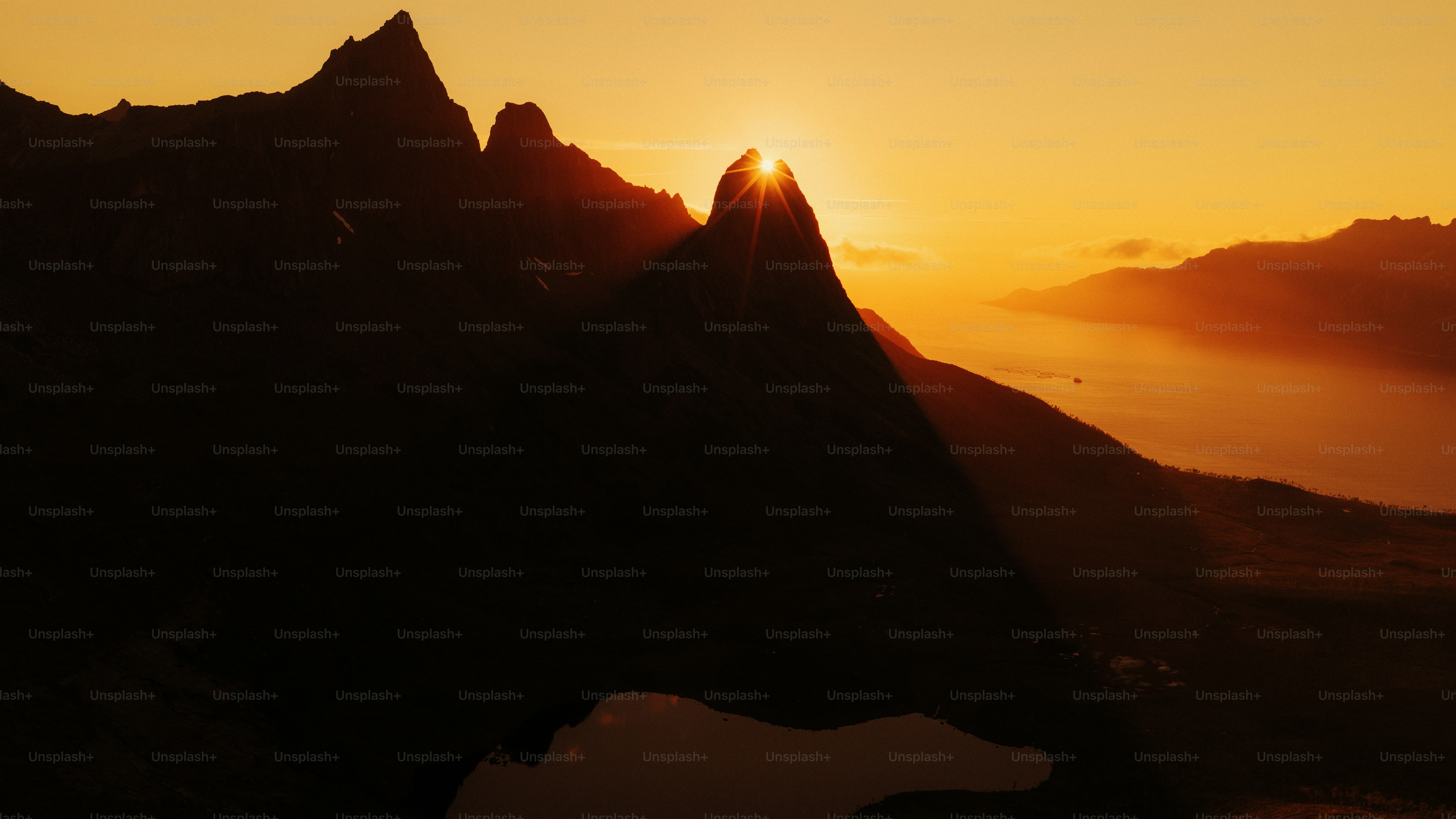 Sun setting behind jagged mountain peaks and lake