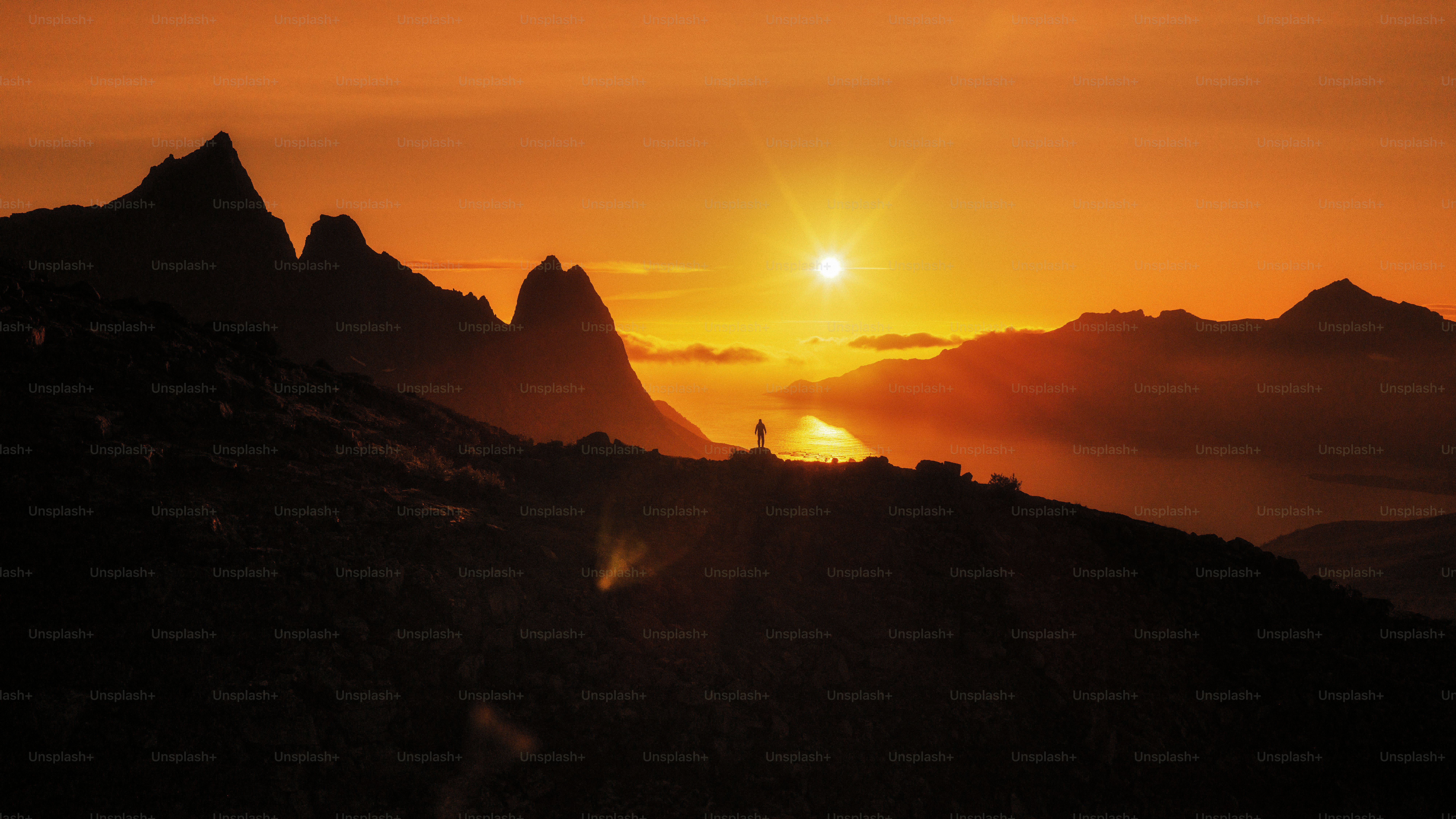Person stands on mountain ridge during vibrant sunset
