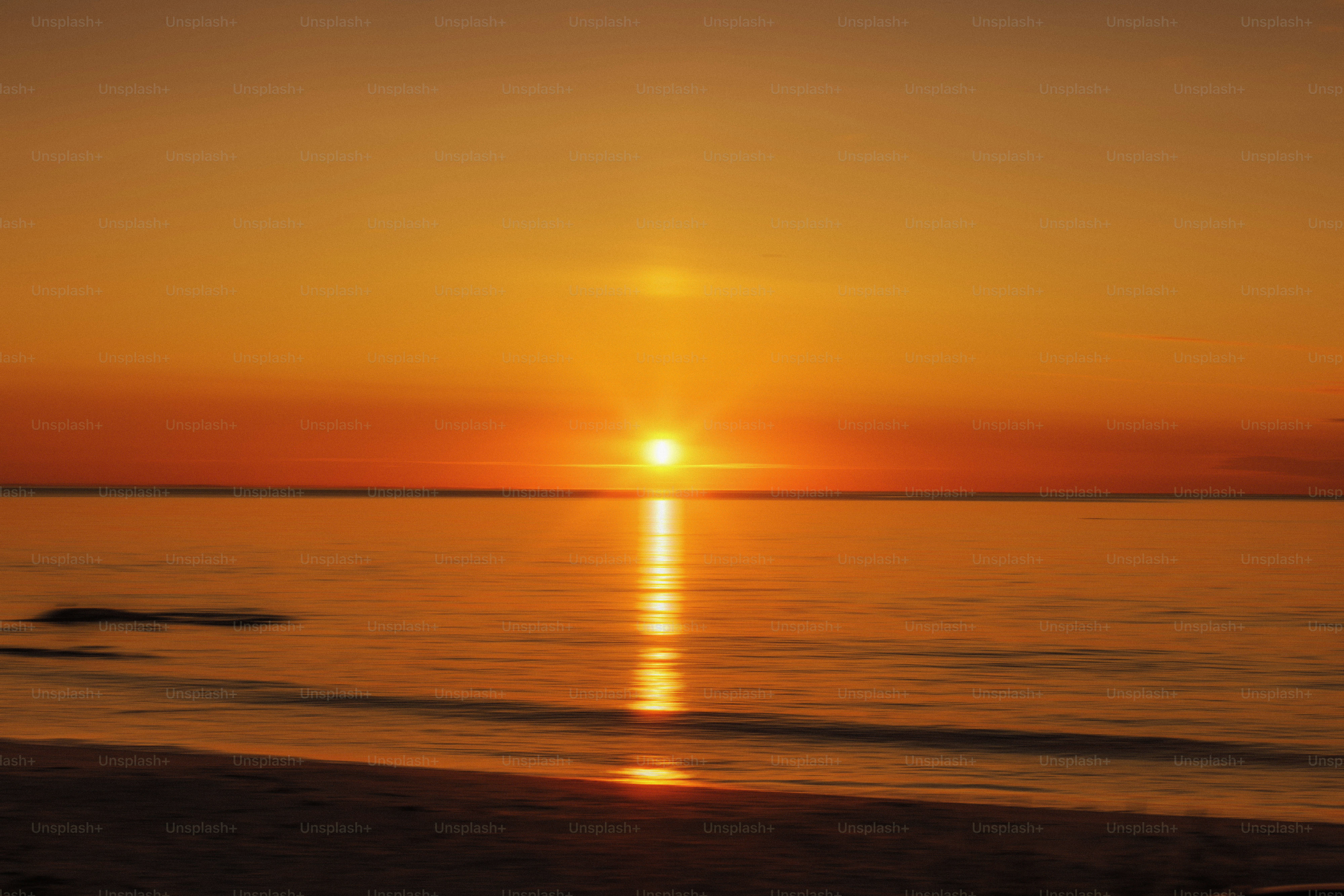 鮮やかなオレンジ色の夕焼けが穏やかな海に映し出される - Unsplash+に