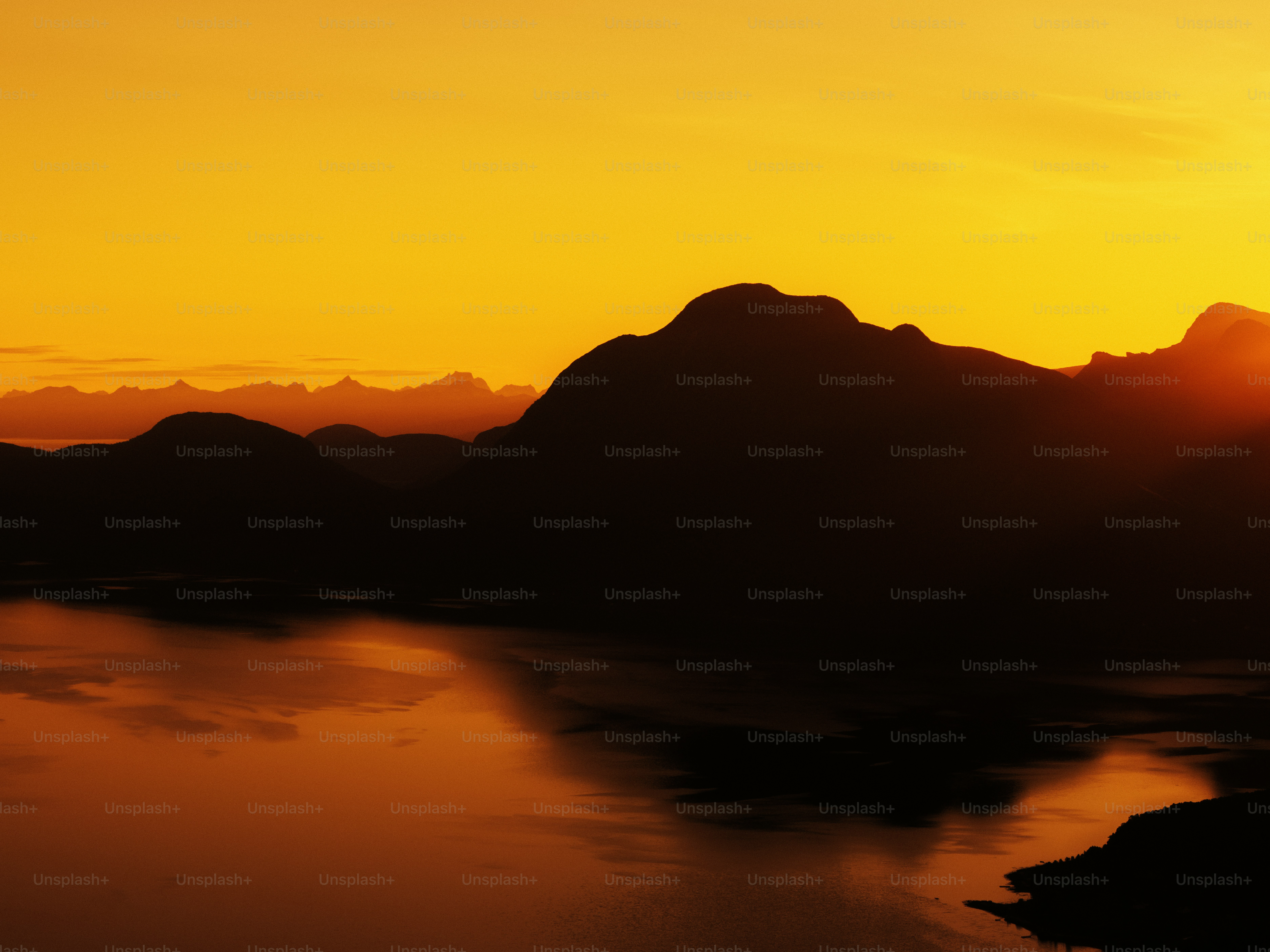 Orange sunset silhouetting mountains over calm water