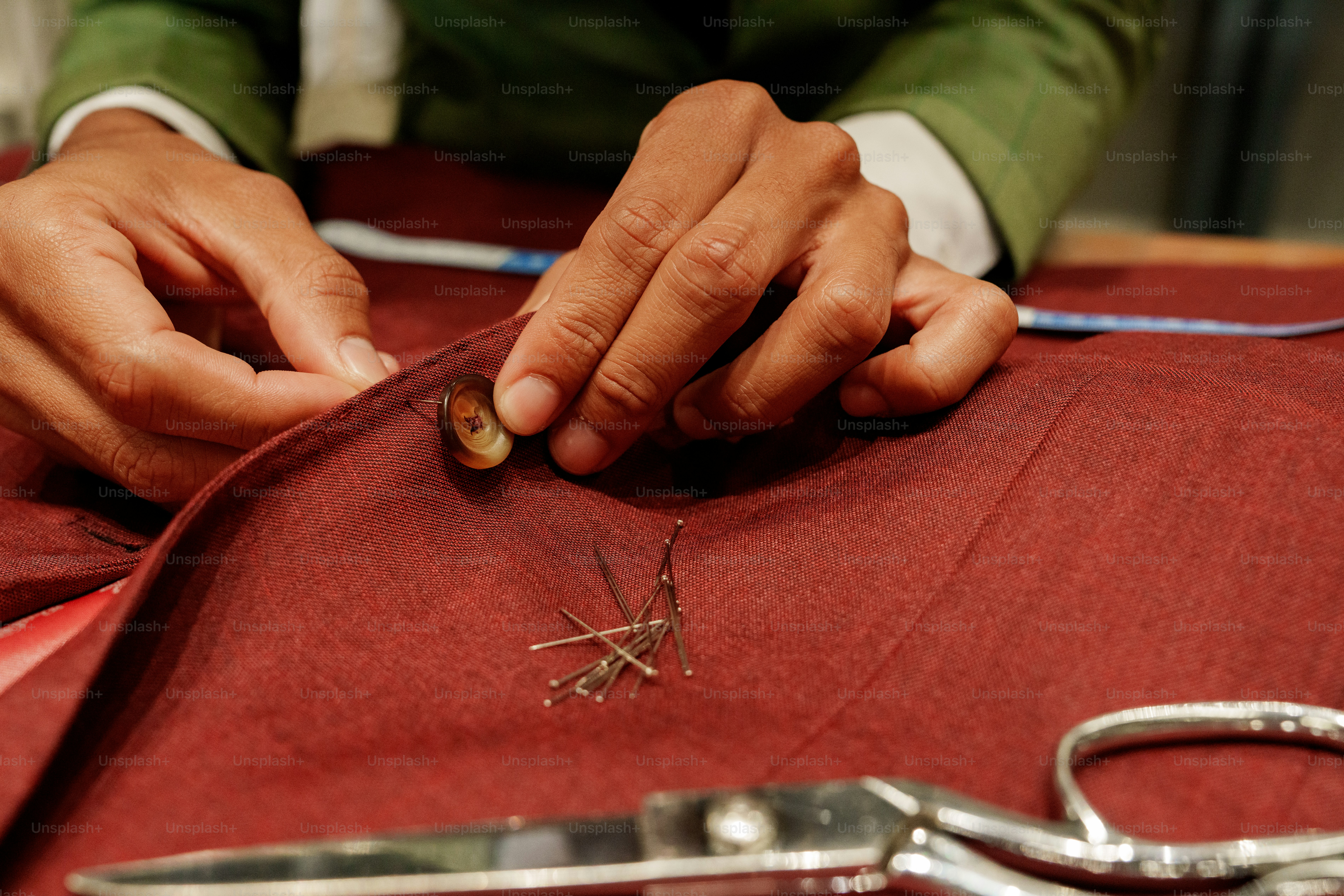 Hands sewing red fabric with pins and scissors