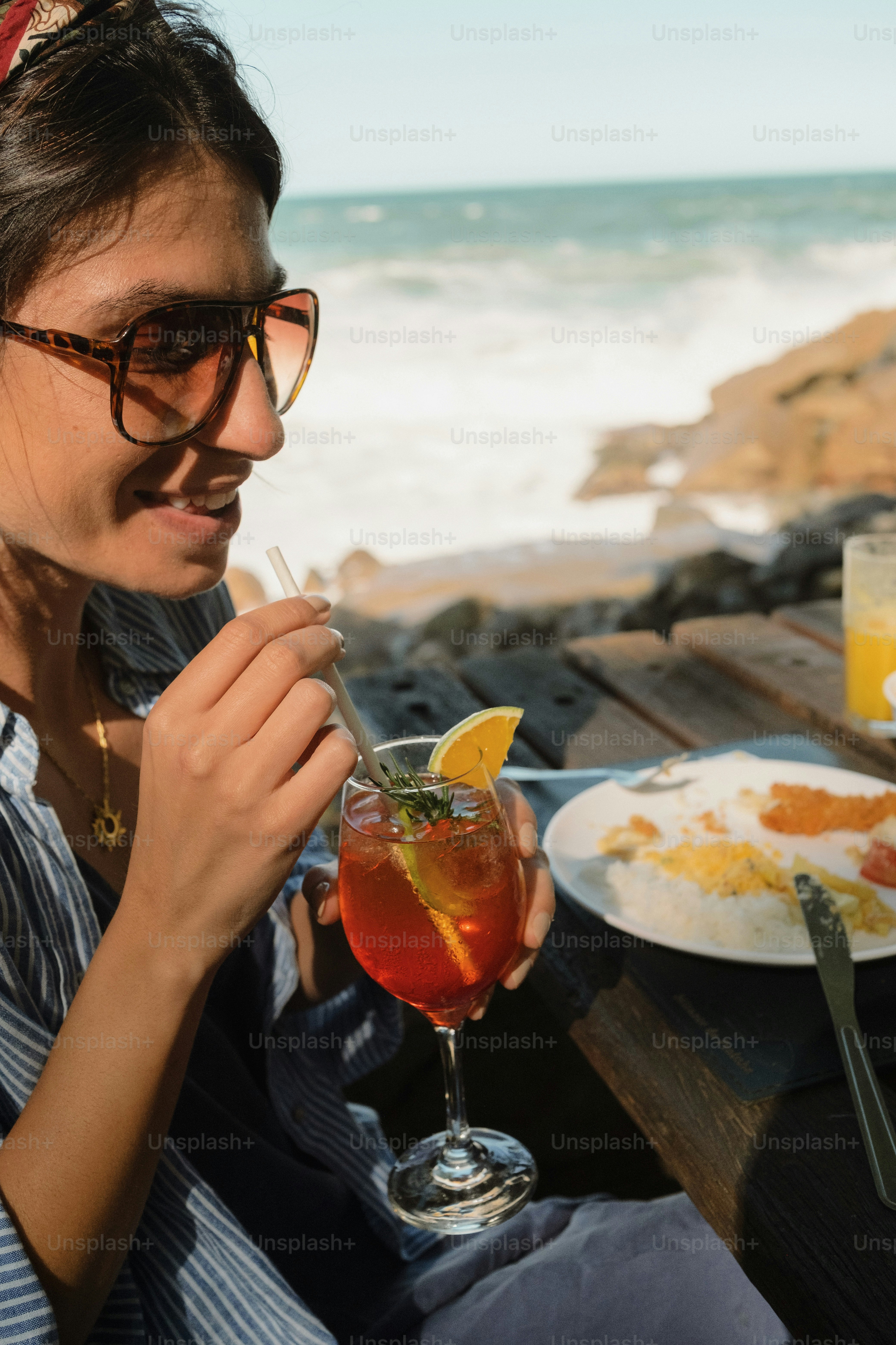 Smiling woman drinking cocktail by ocean