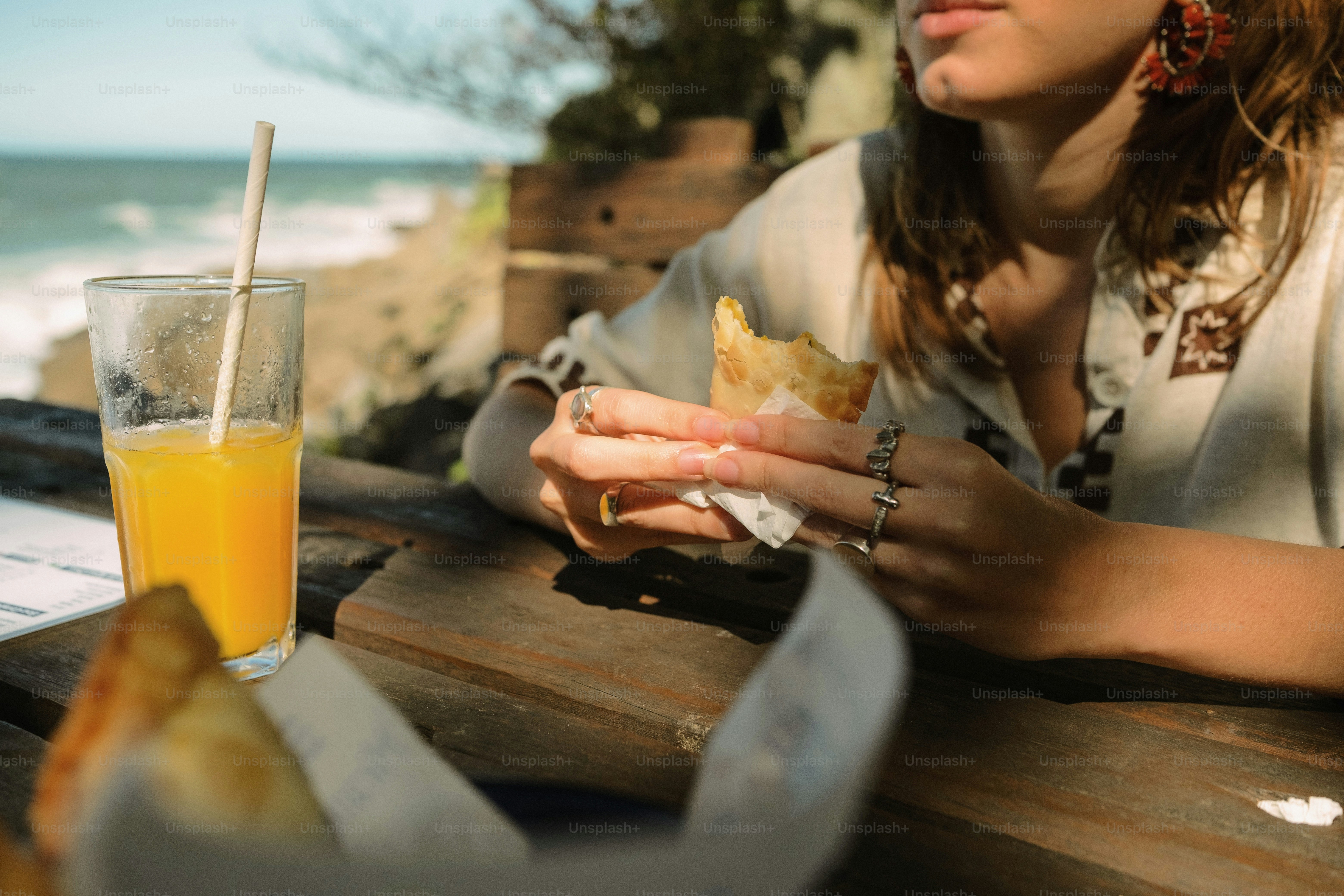 Woman eating pastry with orange juice by the sea