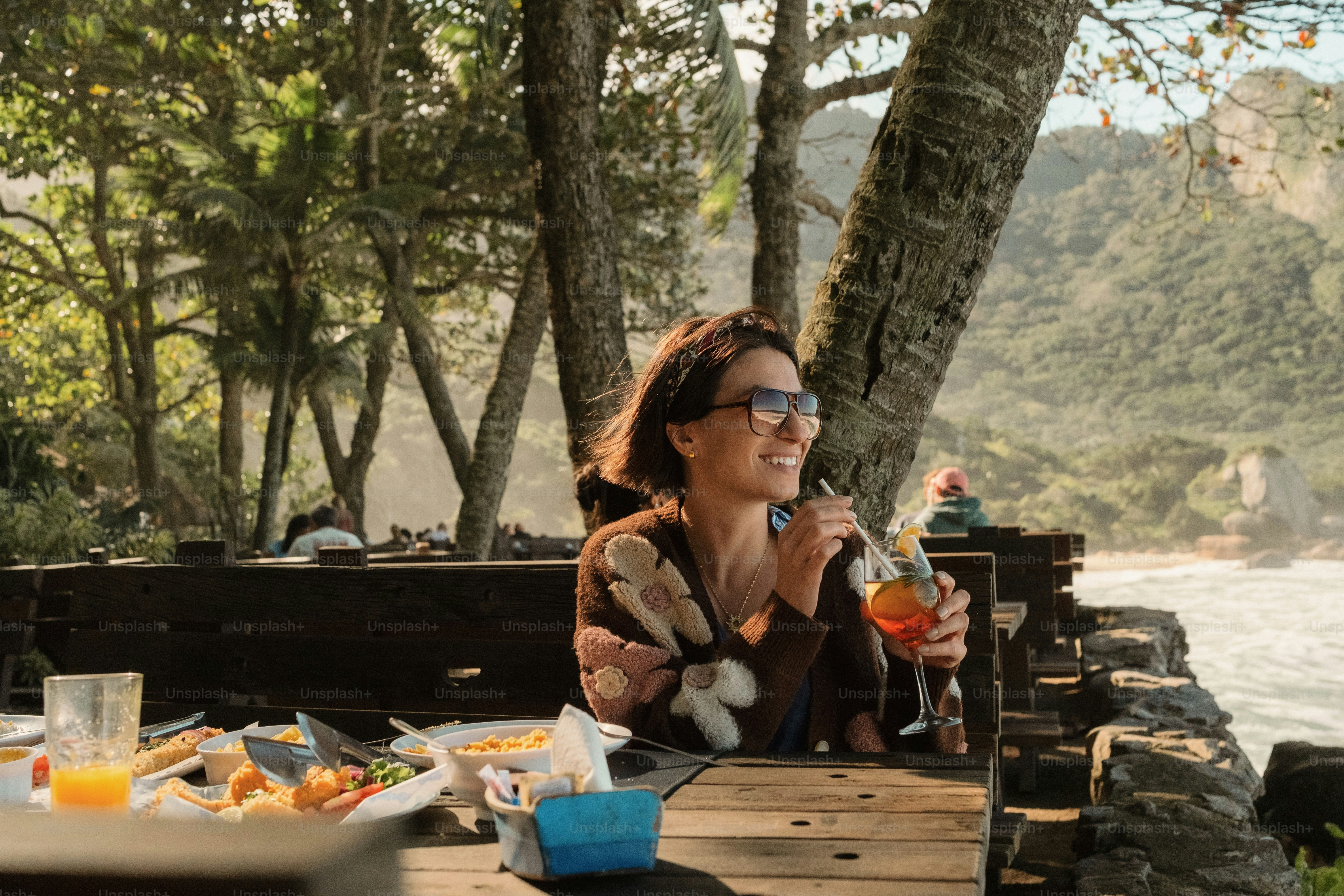 Woman with drink at outdoor table overlooking ocean