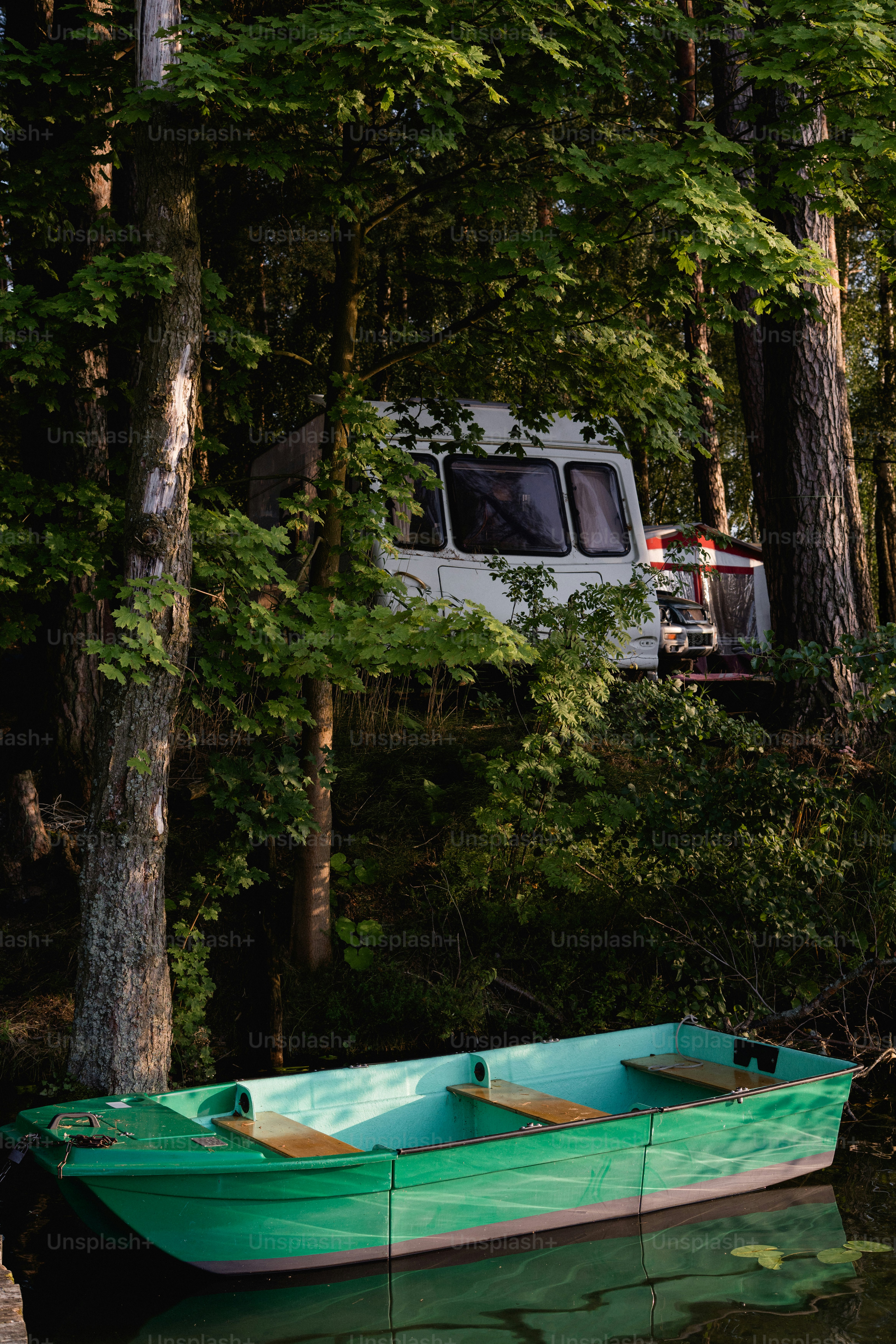 Green rowboat on water, camper van among trees