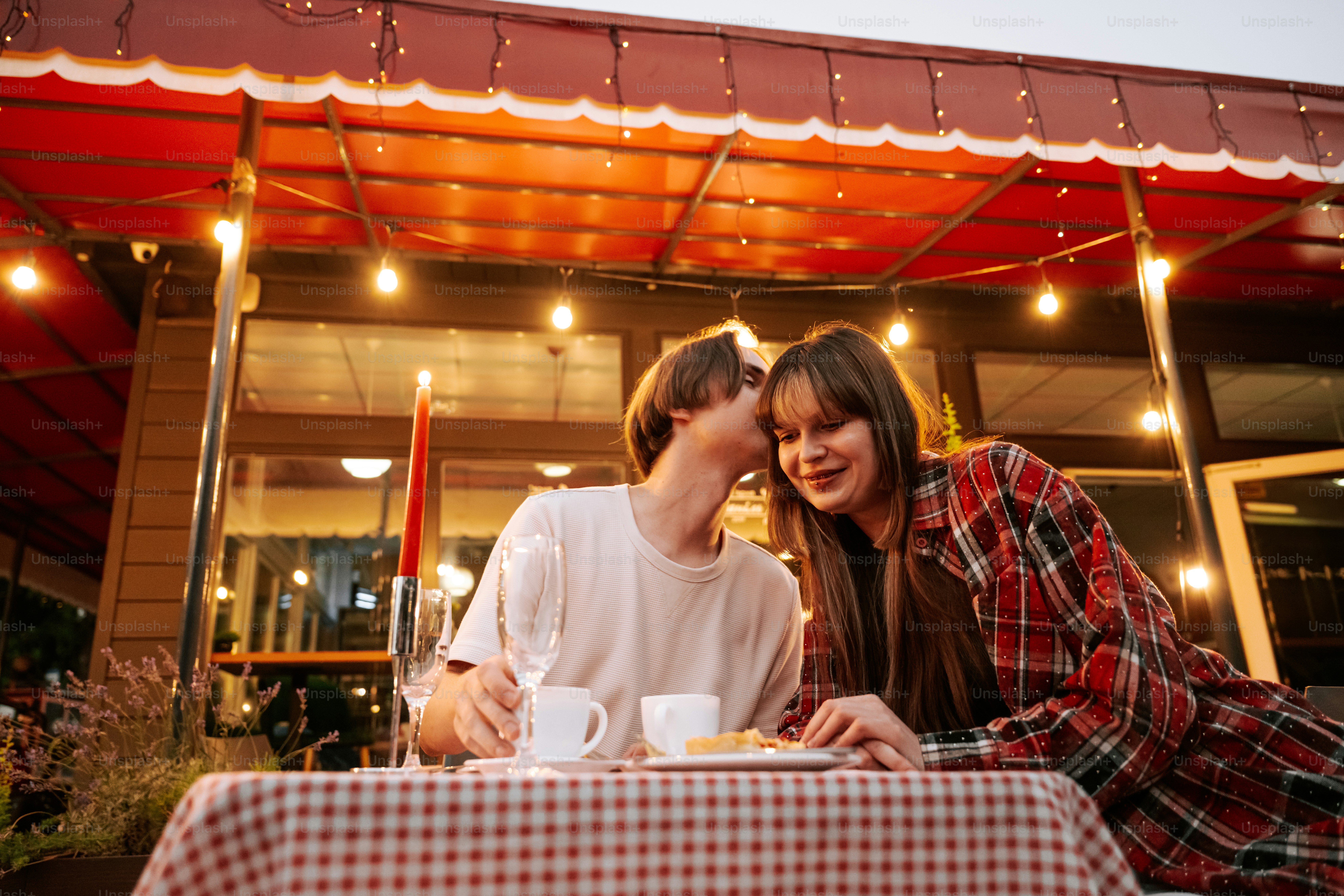 Young couple whispering at outdoor restaurant table