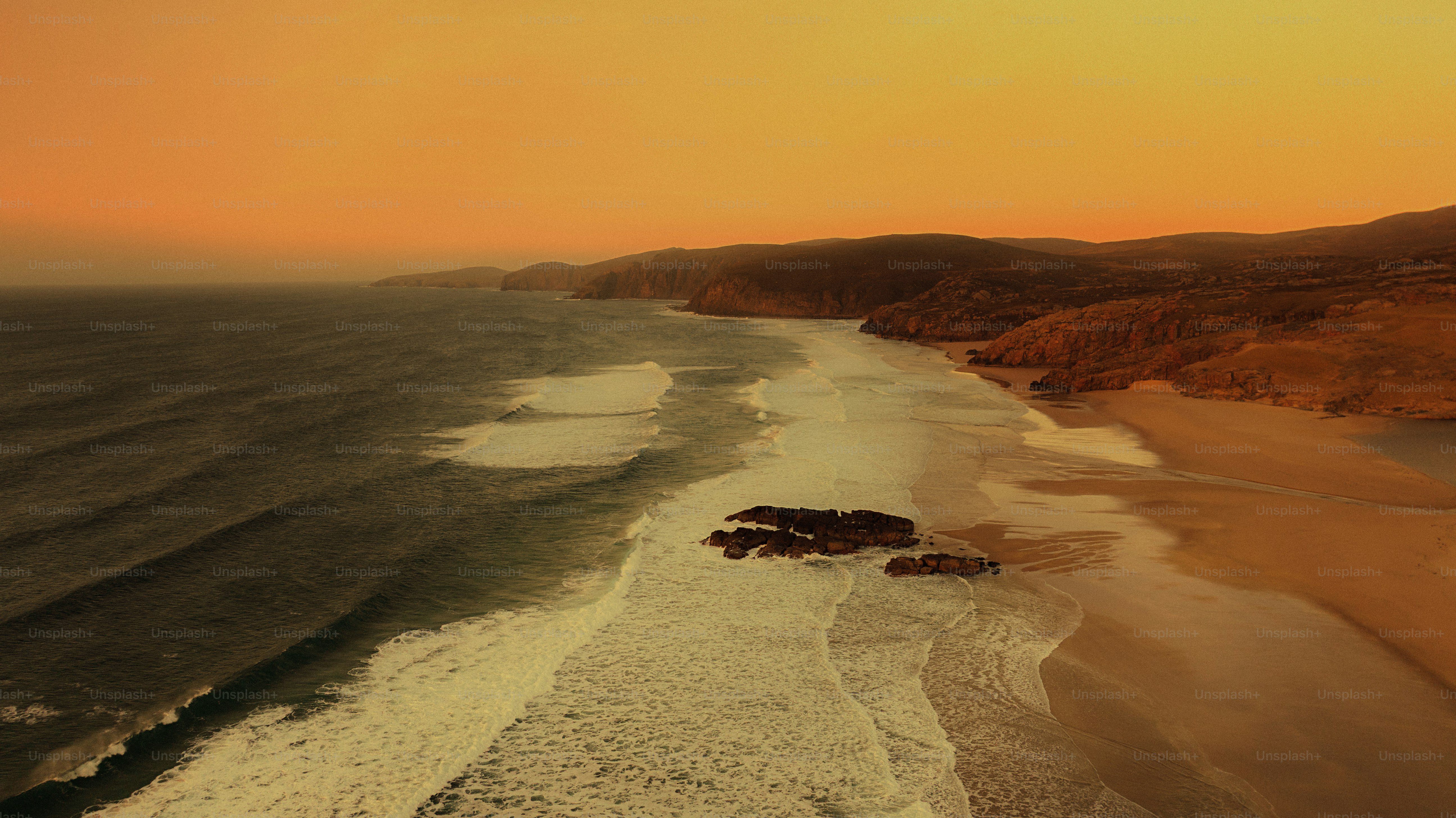 Orange sunset over sandy beach with crashing waves