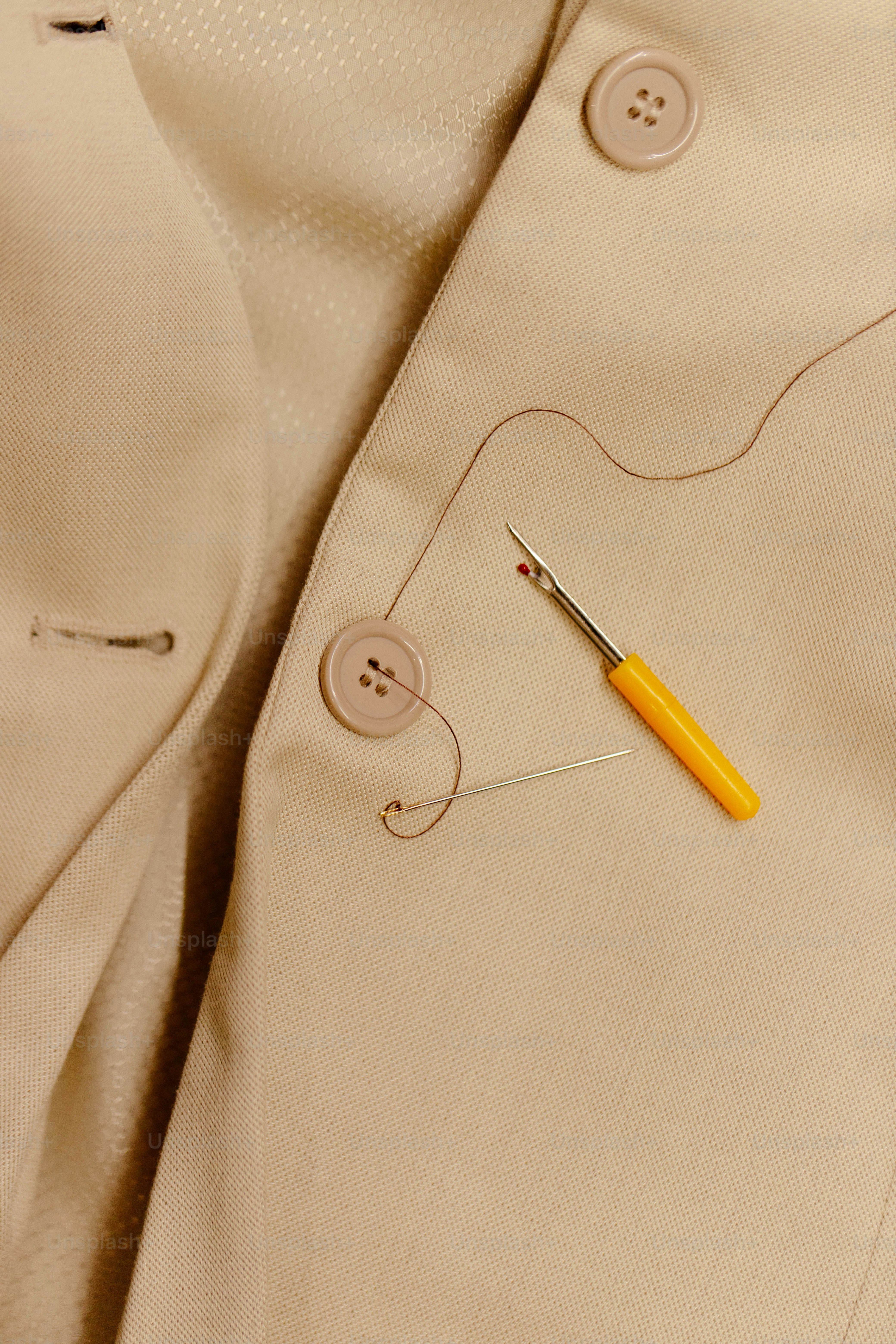 Seam ripper, needle, and thread on beige jacket