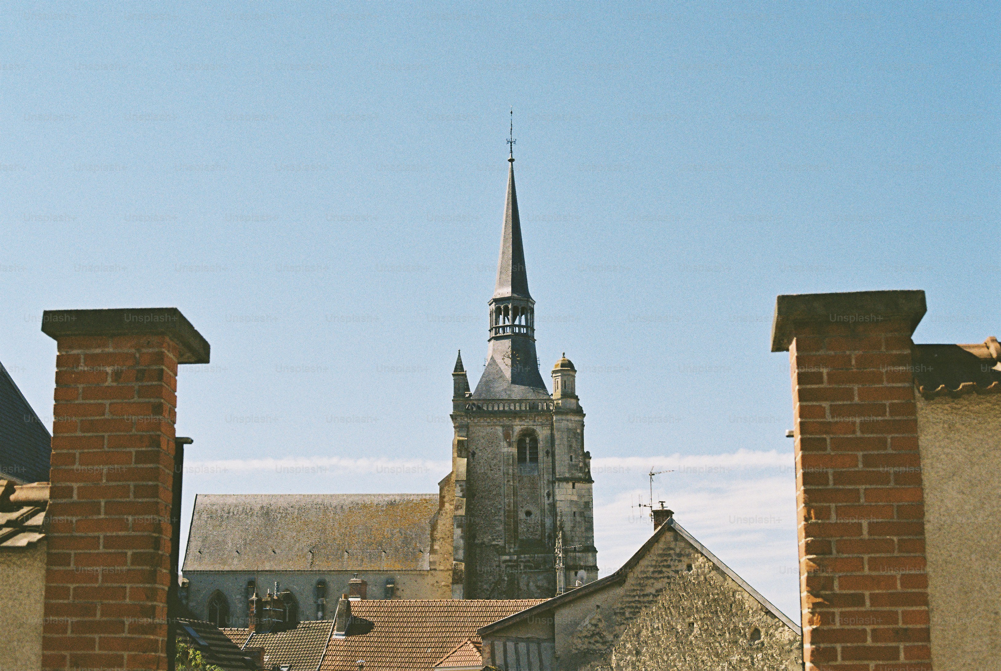 Haute flèche d’église encadrée de piliers et toits en brique