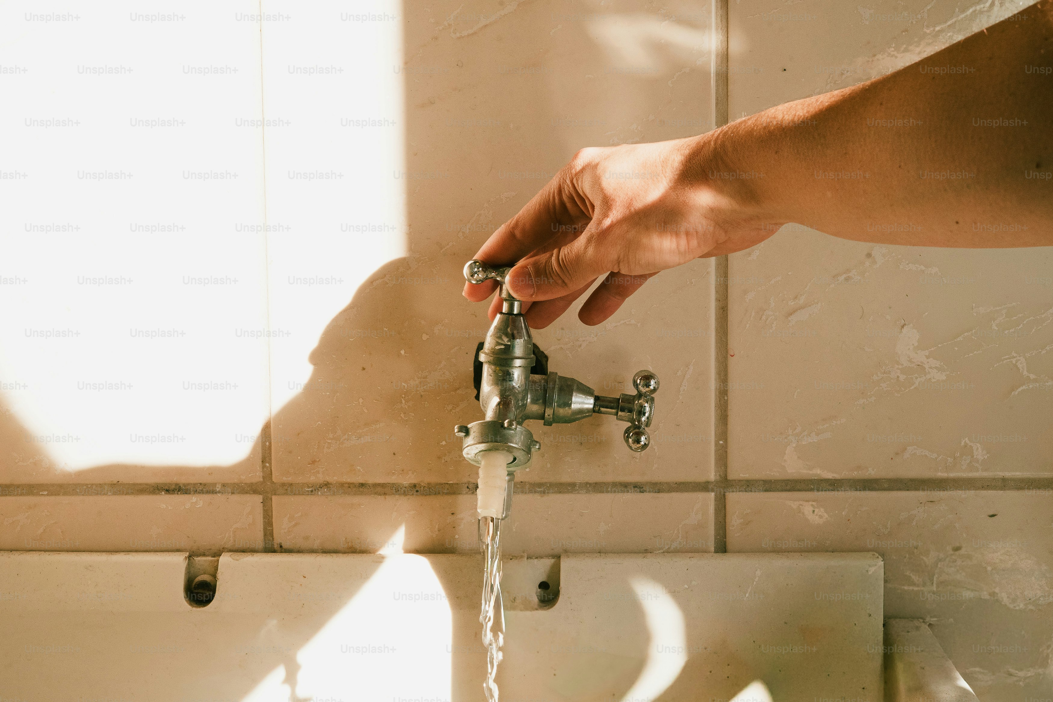 Main qui ouvre le robinet métallique, eau qui coule