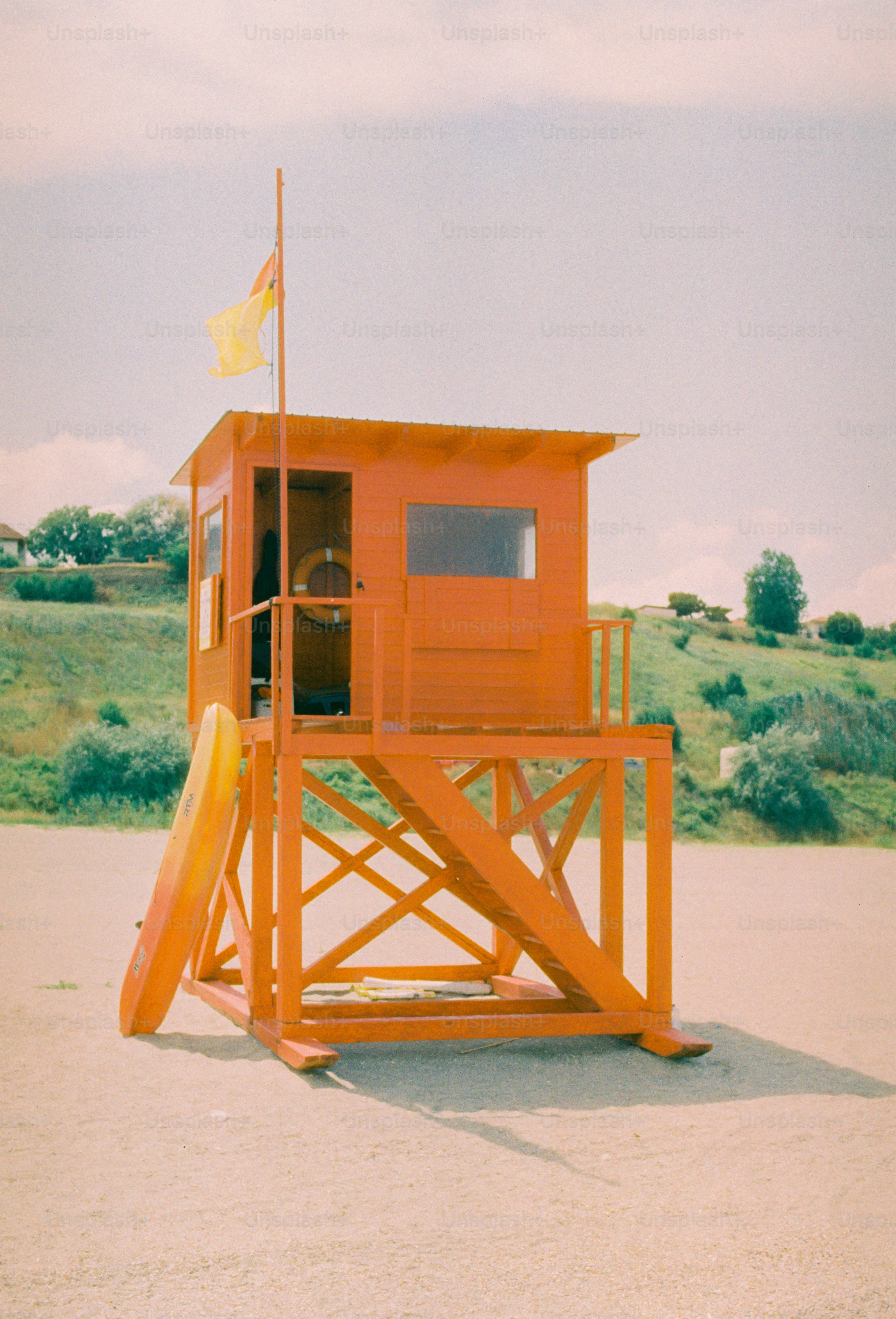 Orange lifeguard tower, yellow flag, surfboard on sandy beach