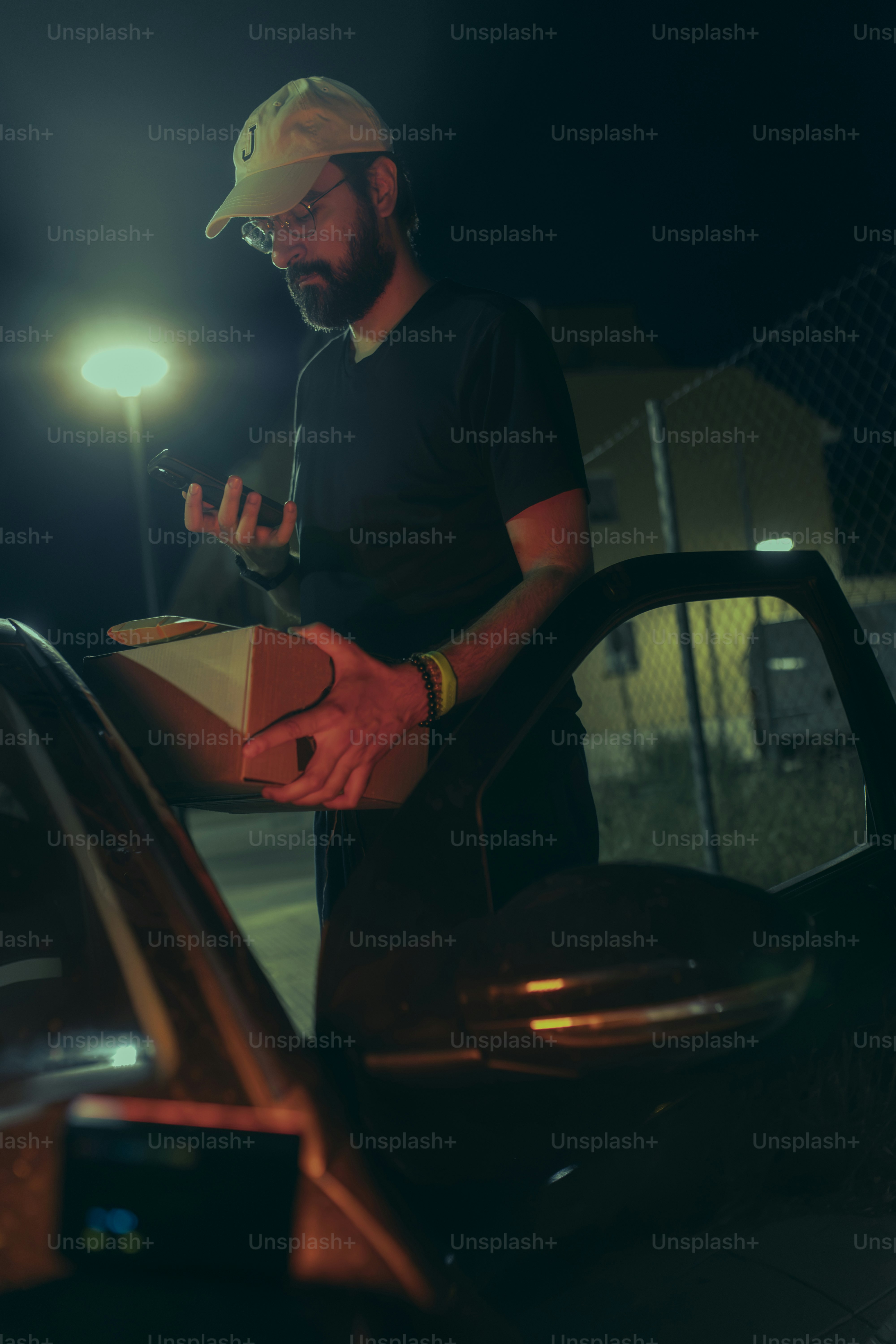 Delivery worker holding parcel and checking details on smartphone during a night shift