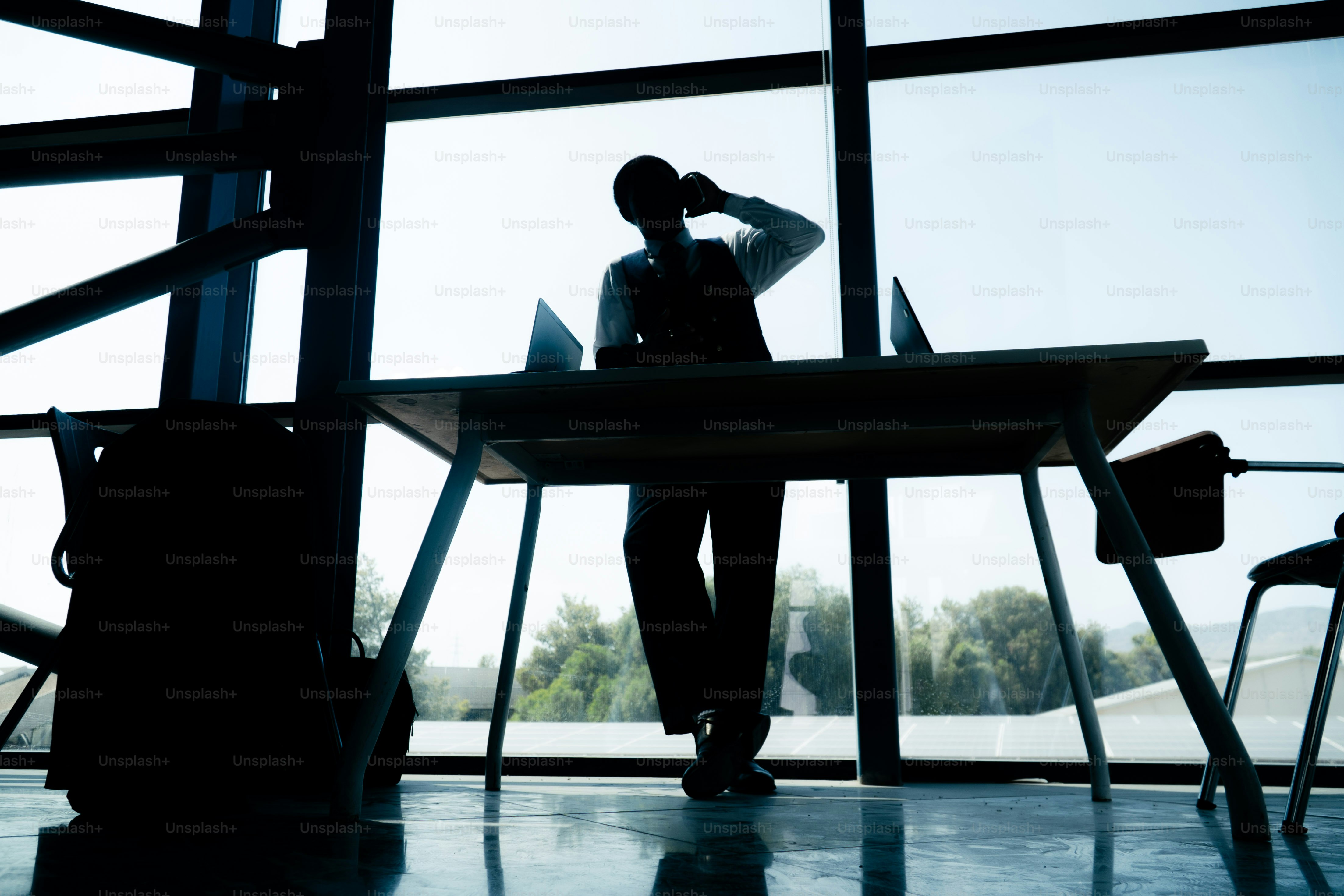 Silhouettenierte Person am Handy am Schreibtisch mit Laptops