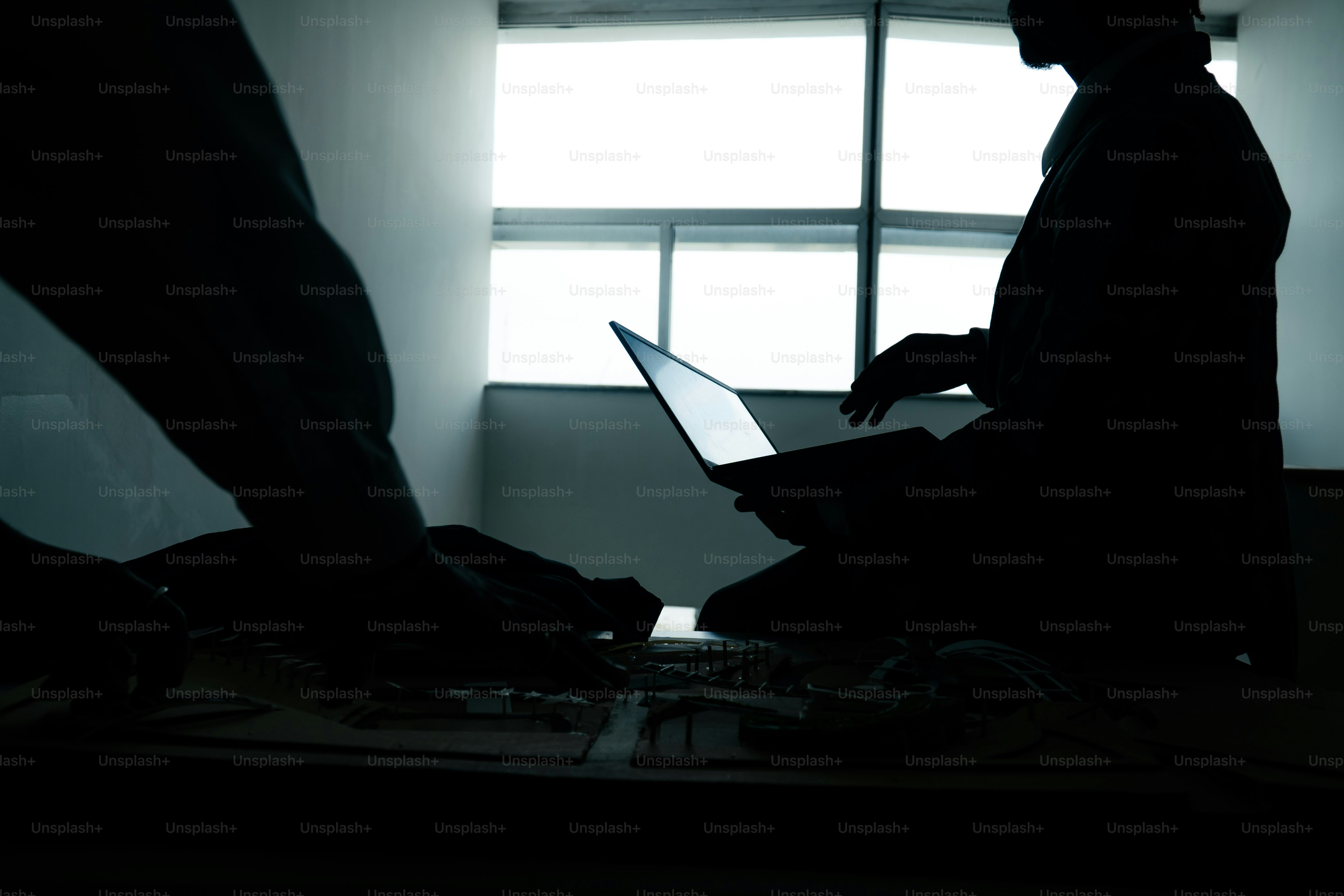 Silhouettenfiguren, die mit dem Laptop im dunklen Raum arbeiten