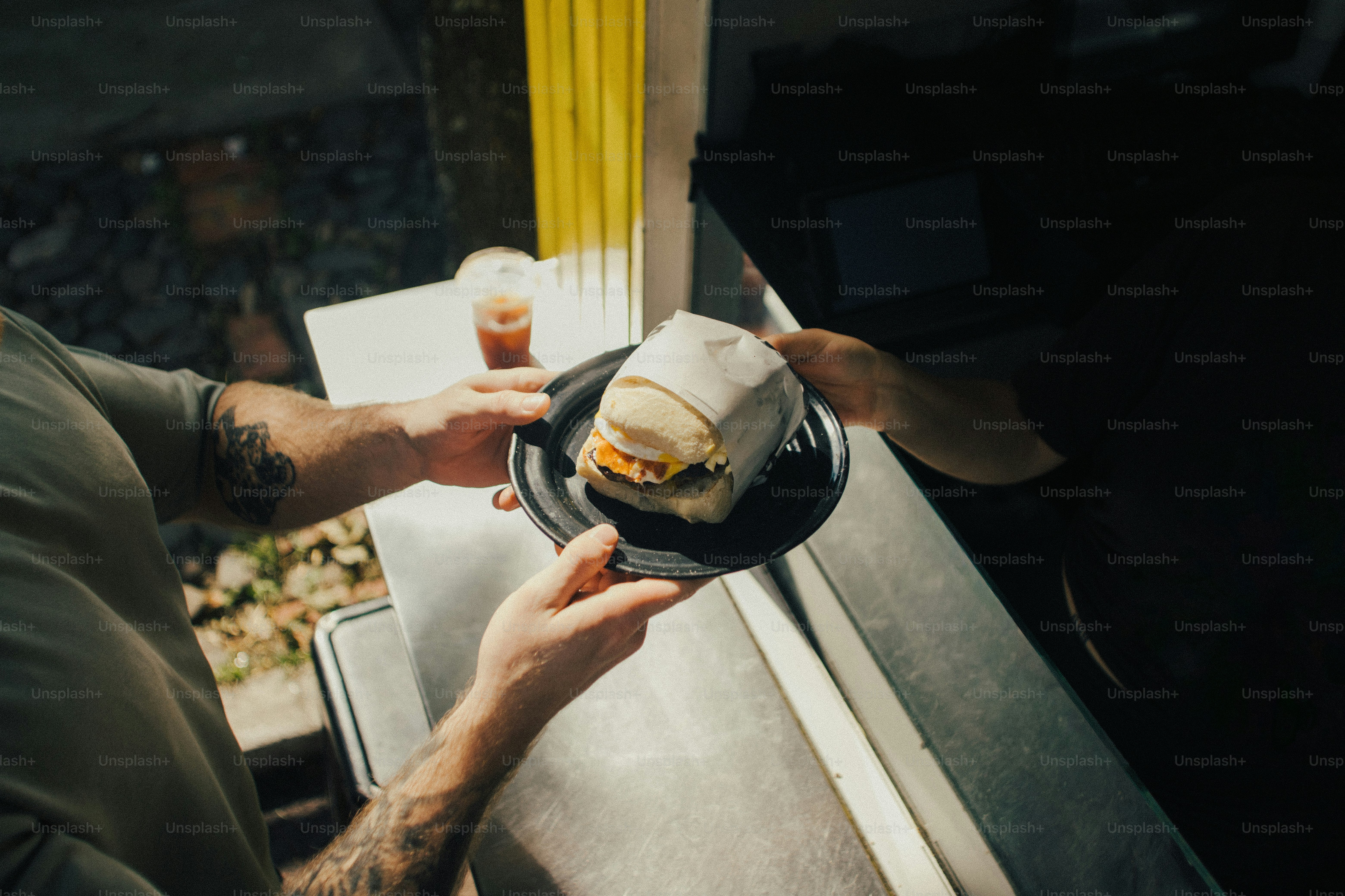 Hands passing a wrapped sandwich on a plate