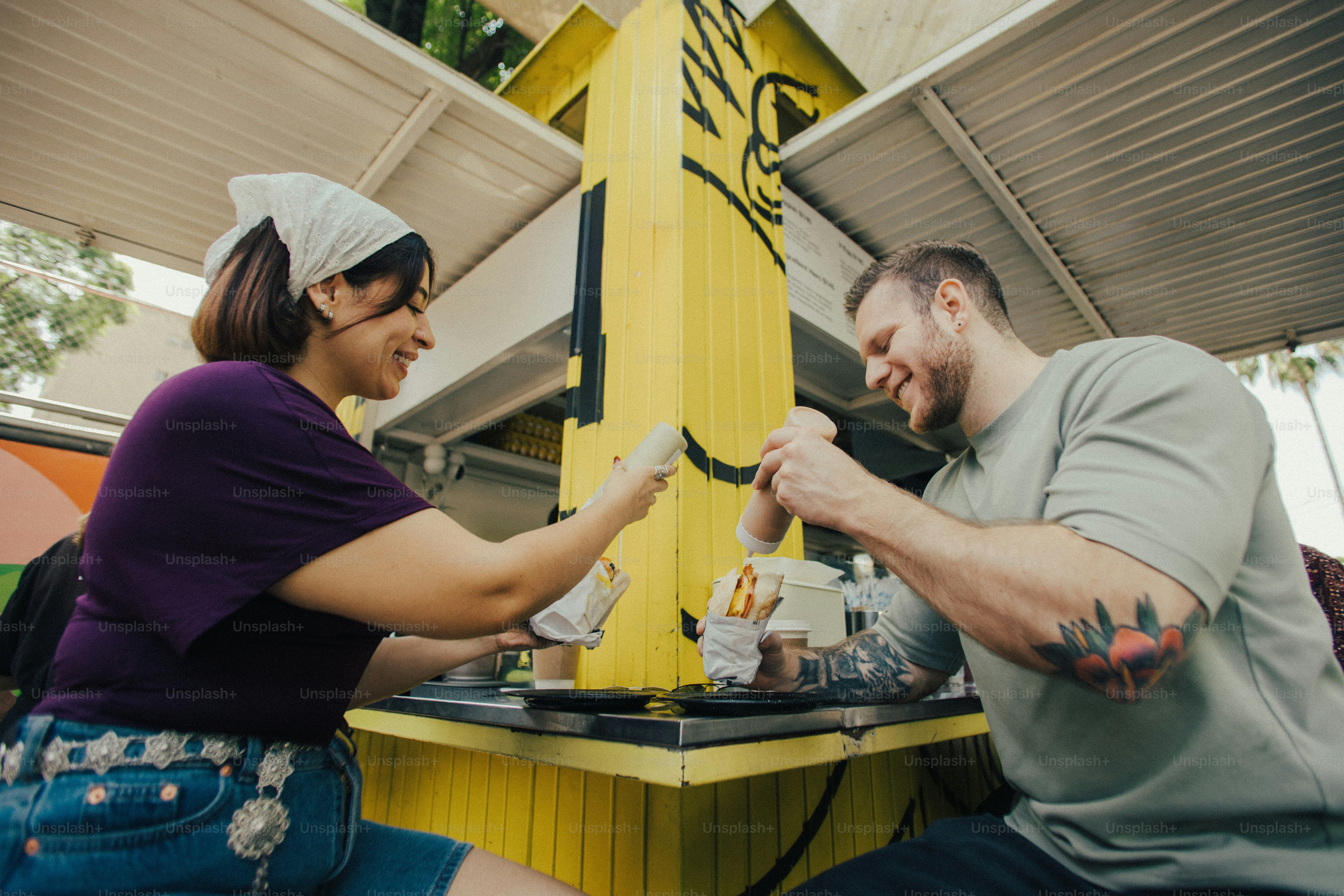 Smiling man and woman eating at a yellow outdoor counter