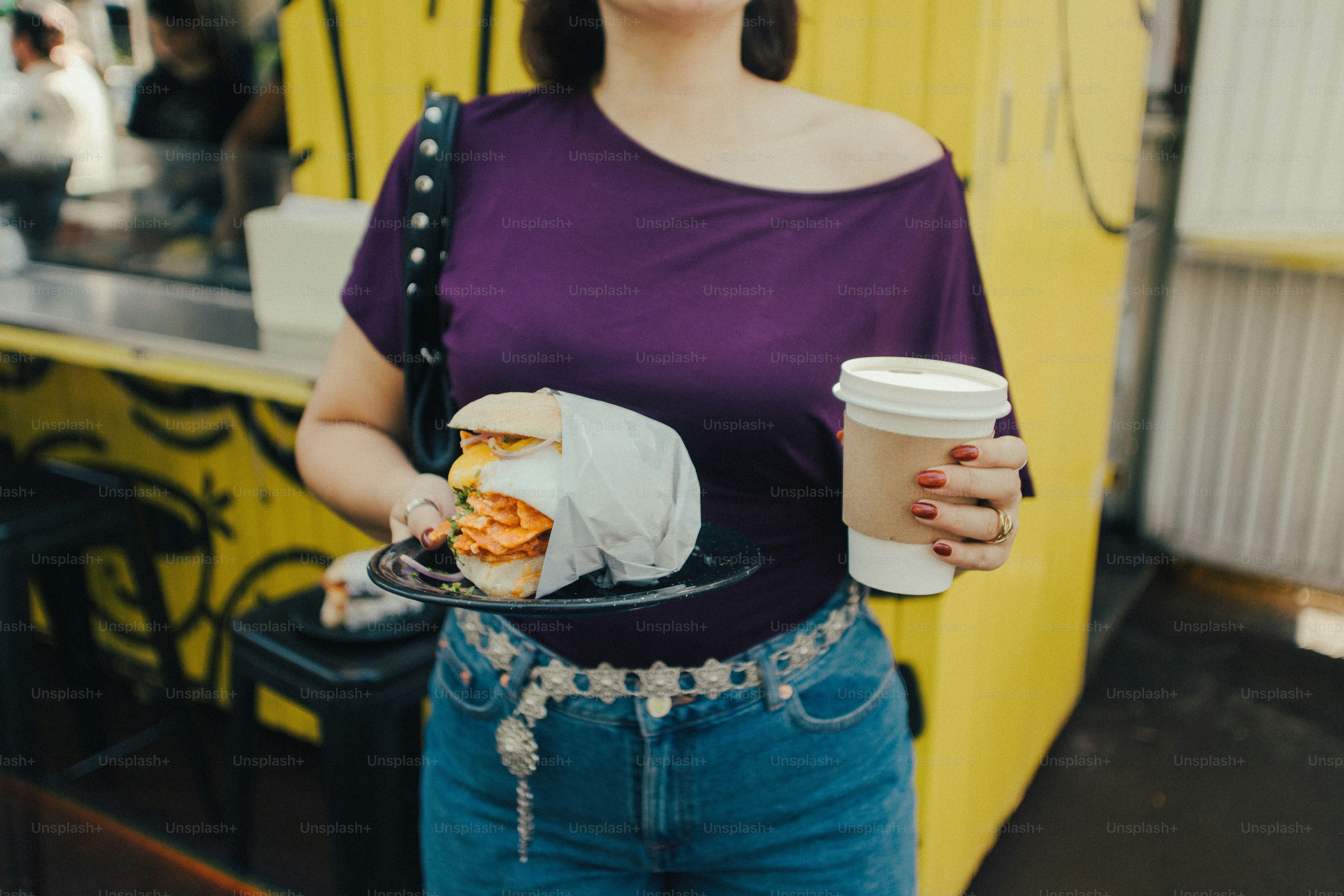Woman holding sandwich and coffee near yellow food truck