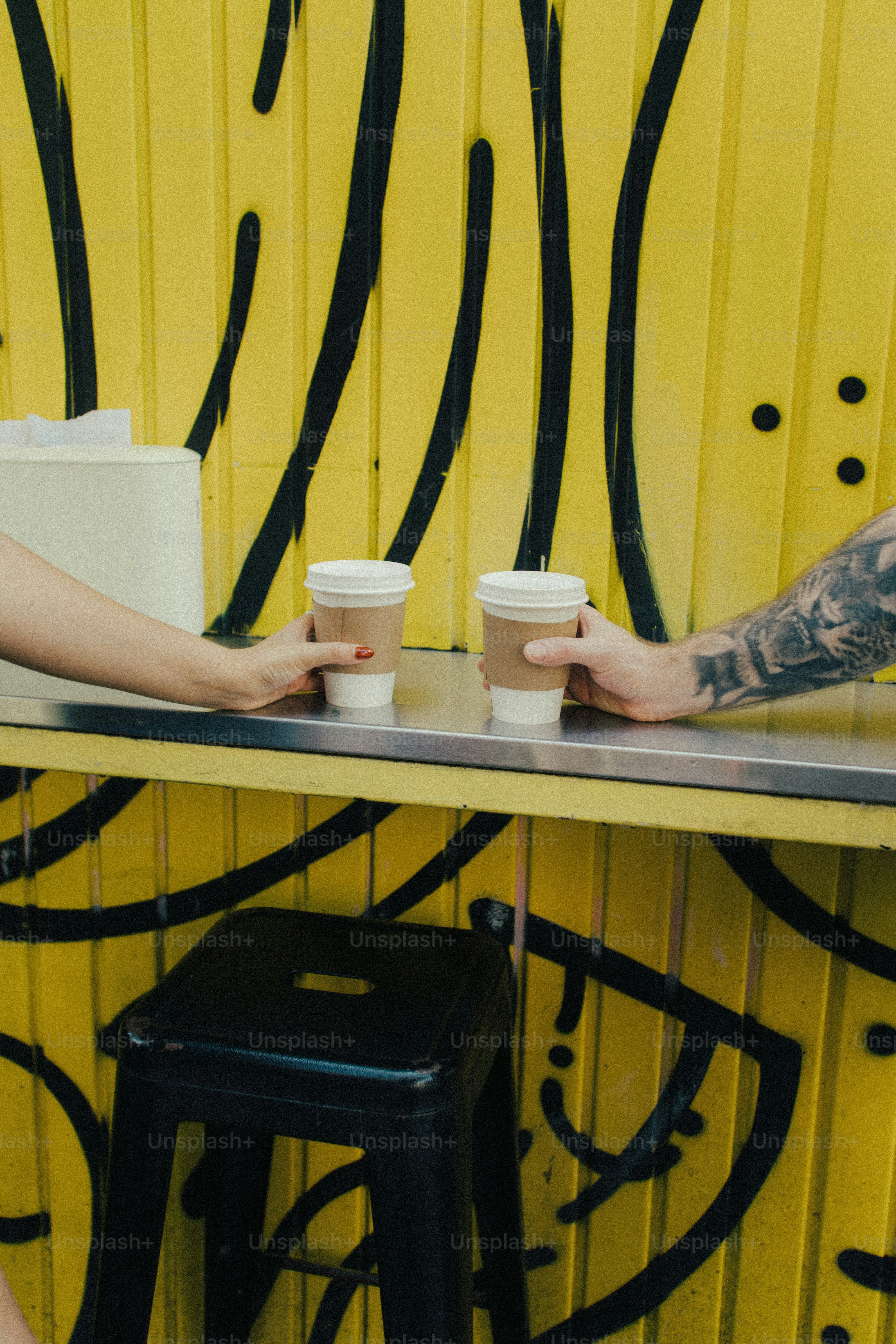 Hands holding coffee cups against yellow graffiti wall