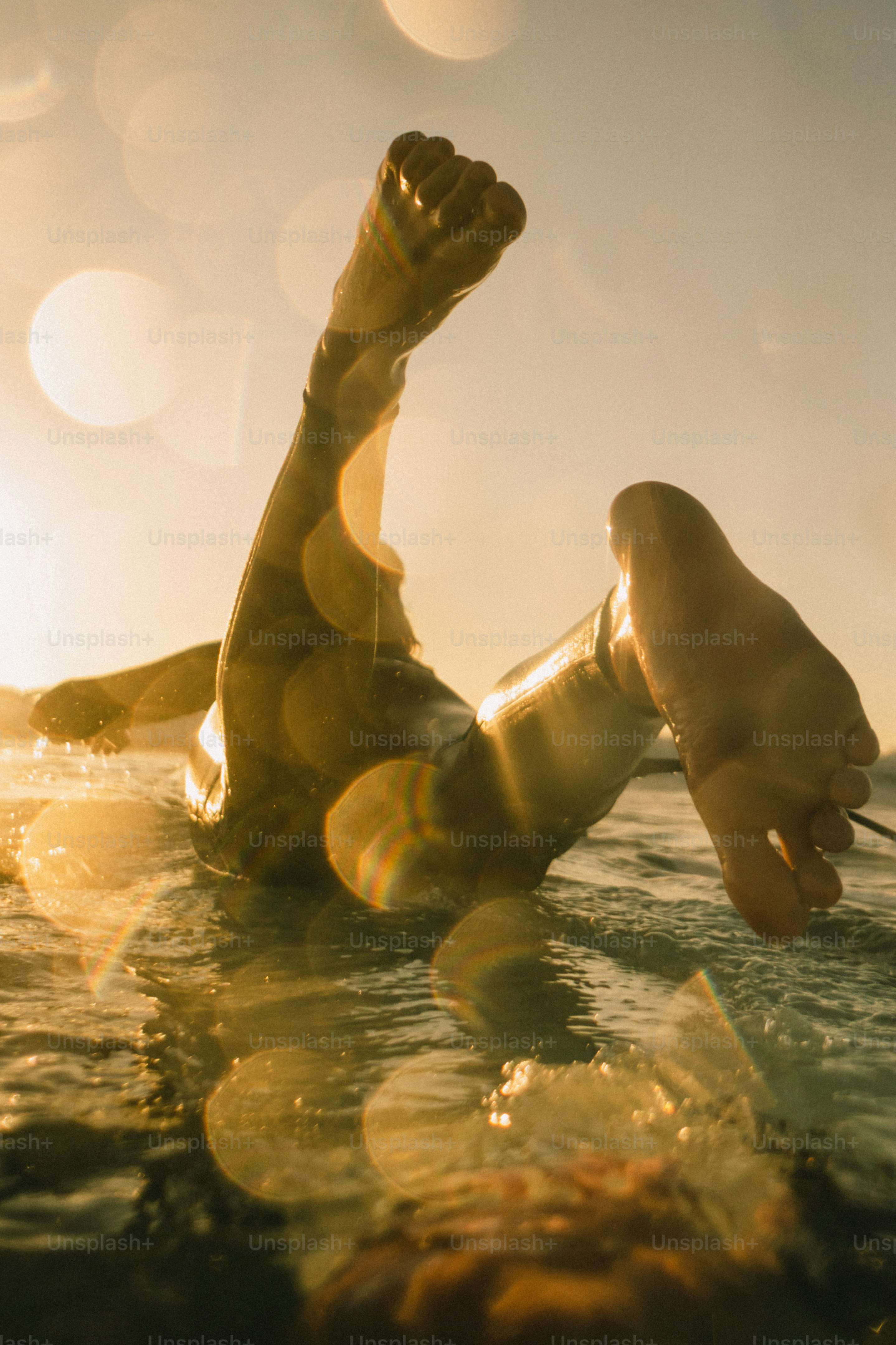 Surferbeine im Wasser während goldenen Sonnenuntergangs