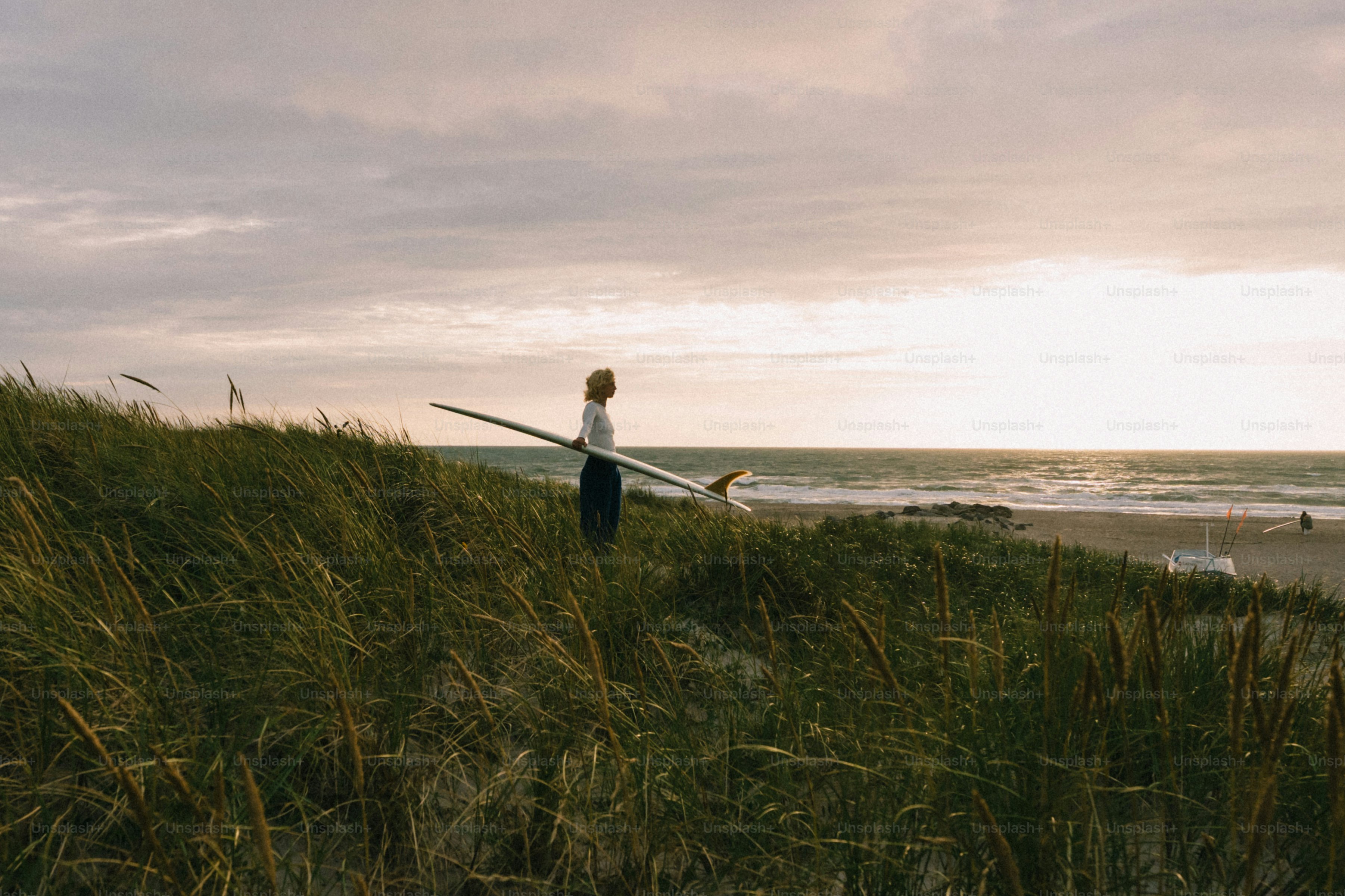 Surfer auf einer grasbewachsenen Düne mit Blick auf den Ozean bei Einbruch der Dämmerung