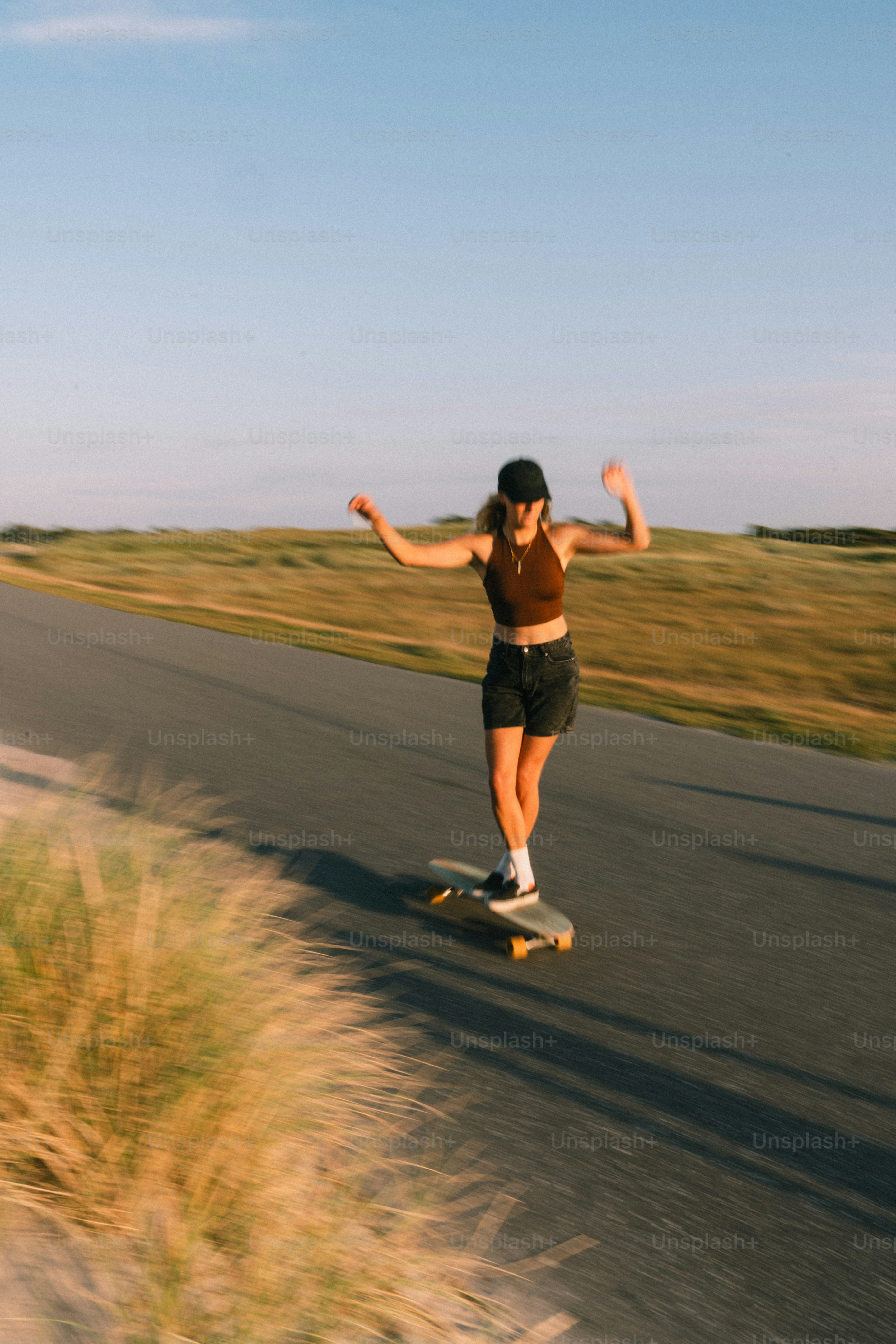 Frau, die auf der Straße durch grasbewachsene Landschaft longboardet