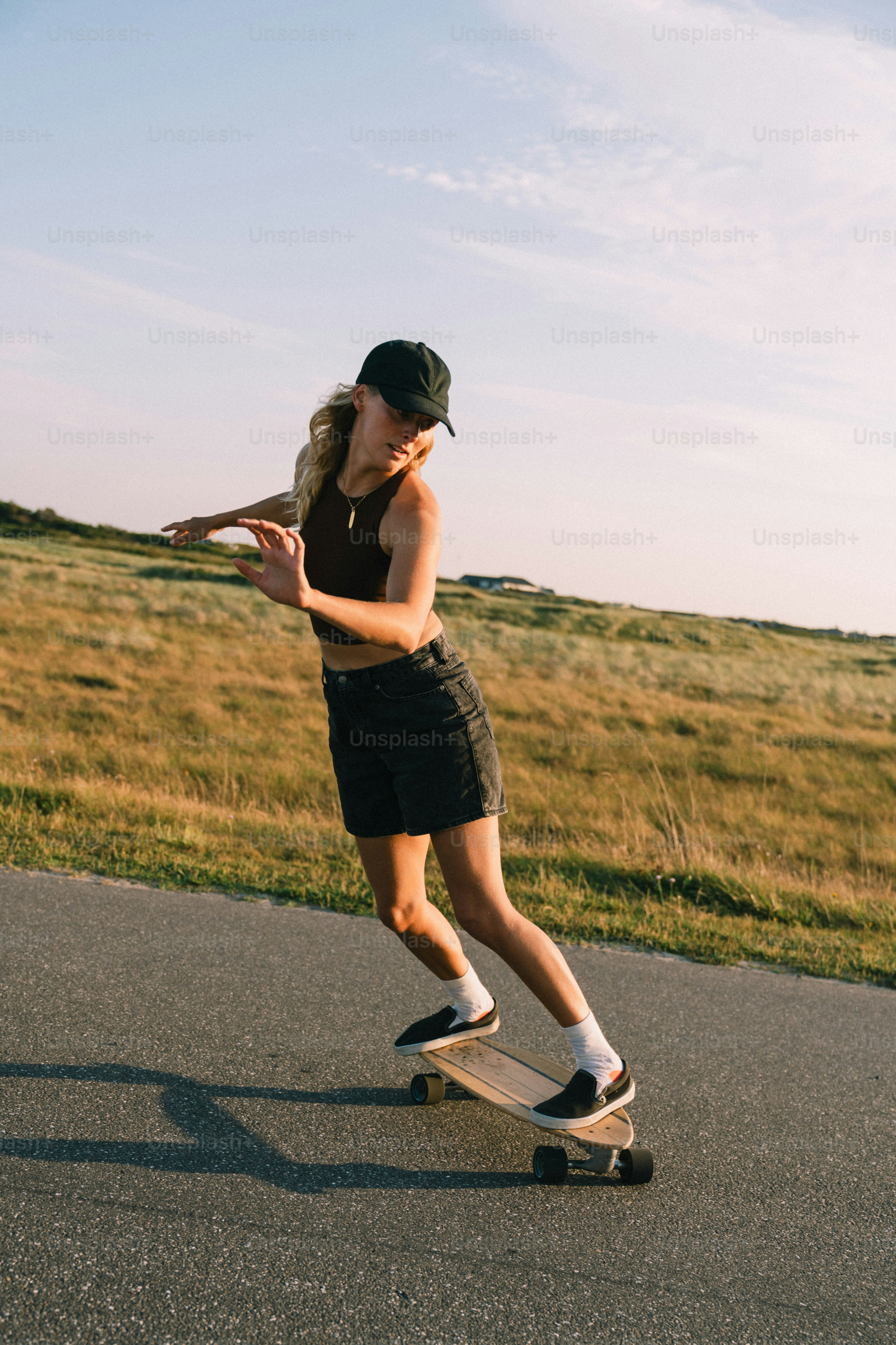 Blonde Frau, die auf dem Weg am Grasfeld Skateboard fährt