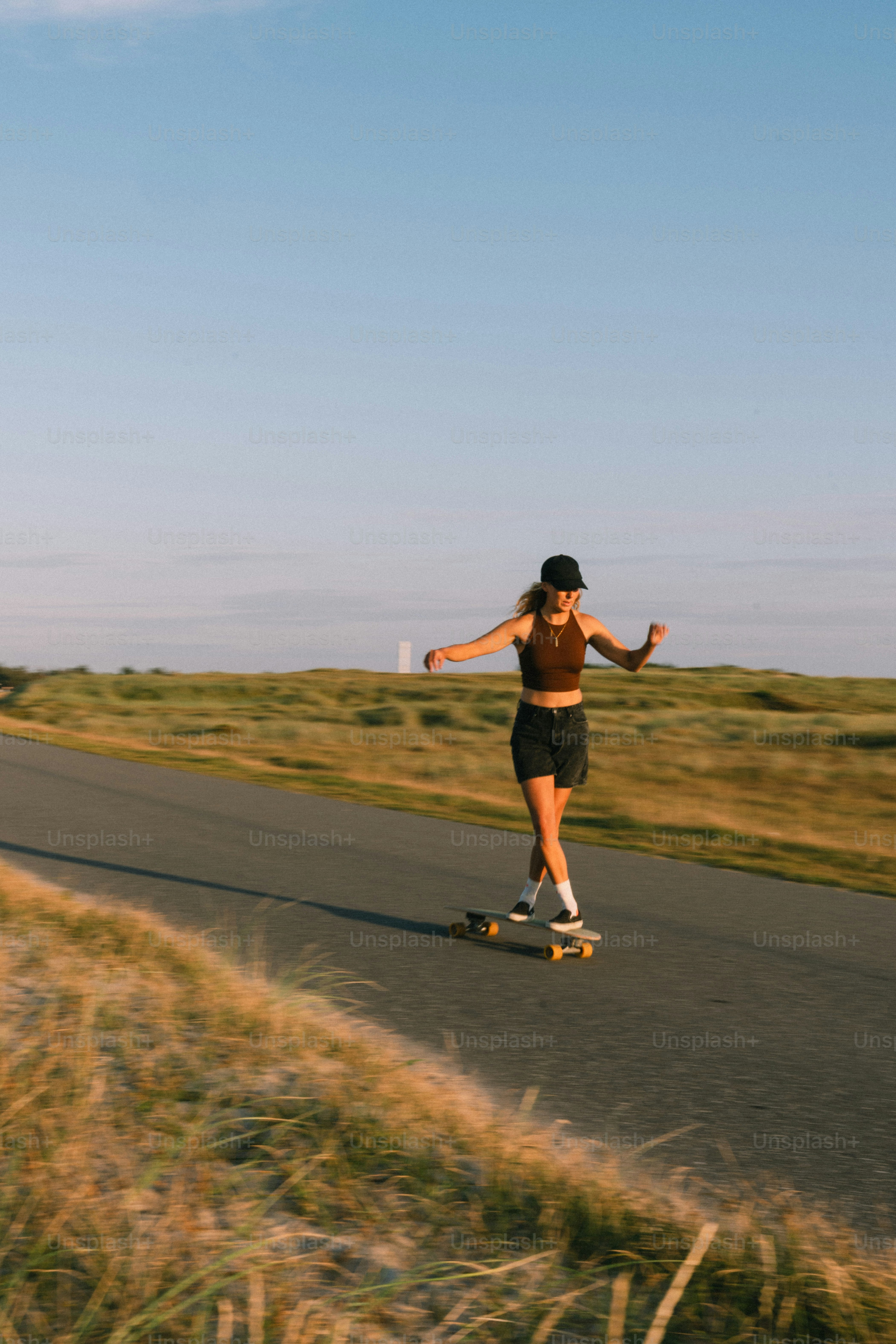 Frau, die auf einer Straße durch grasbewachsene Felder Skateboard fährt