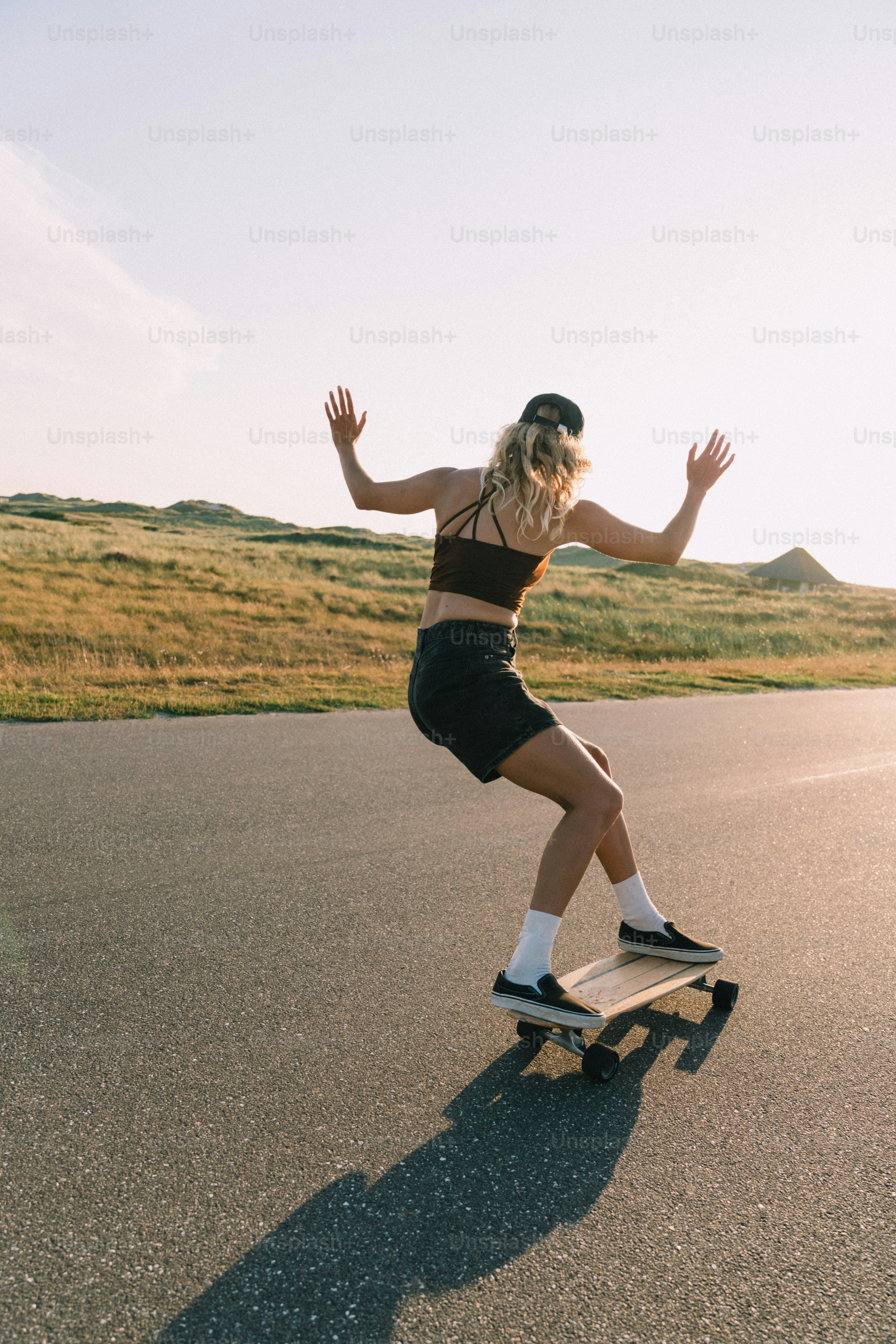 Skater auf der Straße mit grasbewachsenen Hügeln bei Sonnenuntergang